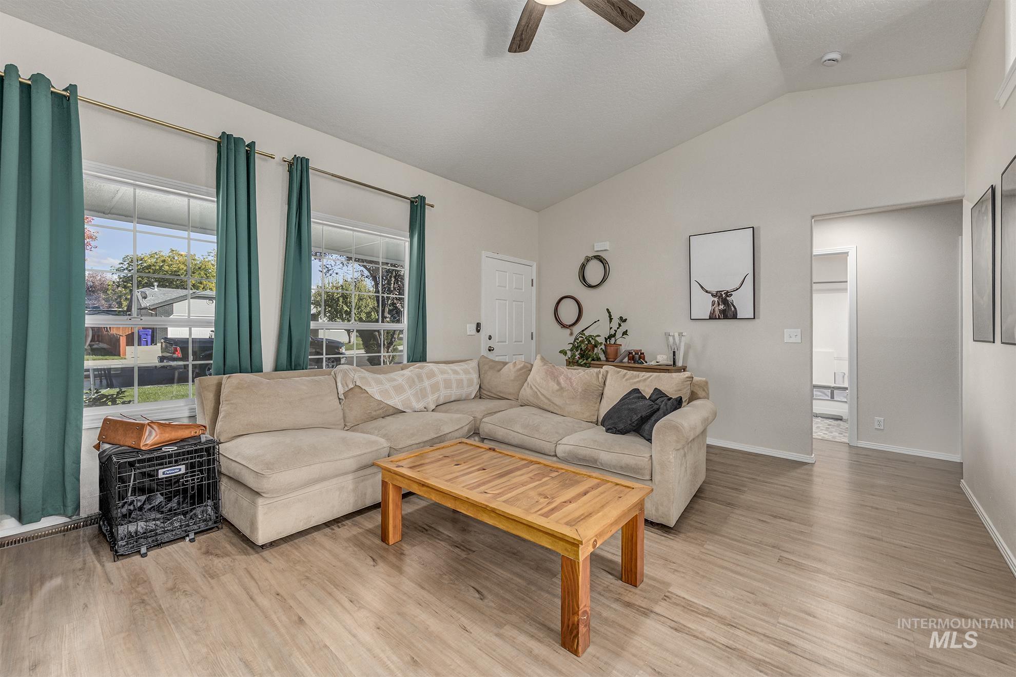Living area featuring vaulted ceiling, light wood-type flooring, a ceiling fan, and a textured ceiling