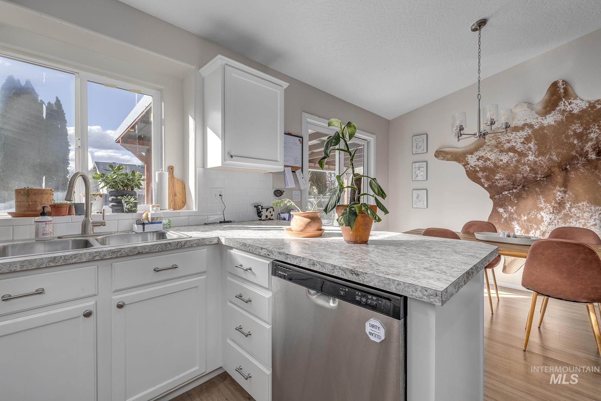 Kitchen featuring white cabinetry, dishwasher, light countertops, decorative backsplash, and light wood finished floors