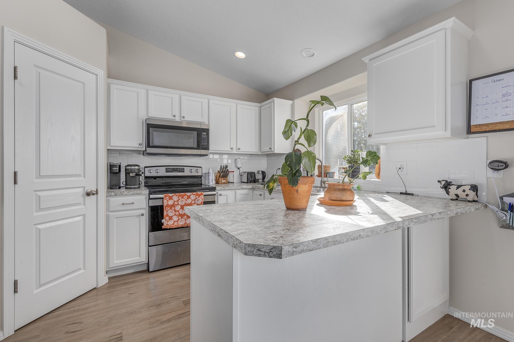 Kitchen with white cabinetry, appliances with stainless steel finishes, tasteful backsplash, a peninsula, and vaulted ceiling