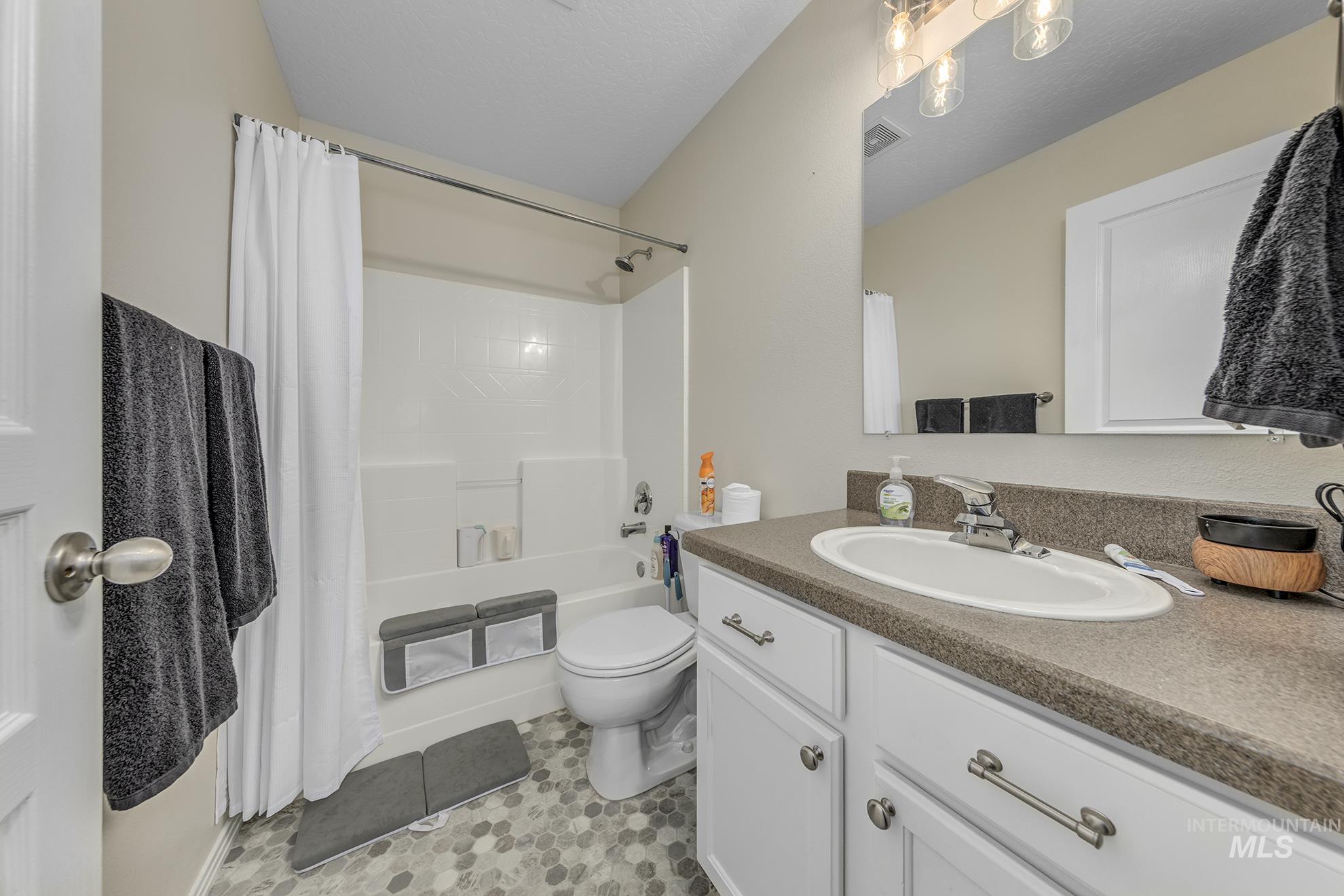 Full bathroom featuring shower / bathtub combination with curtain, vanity, a textured ceiling, and light tile patterned floors