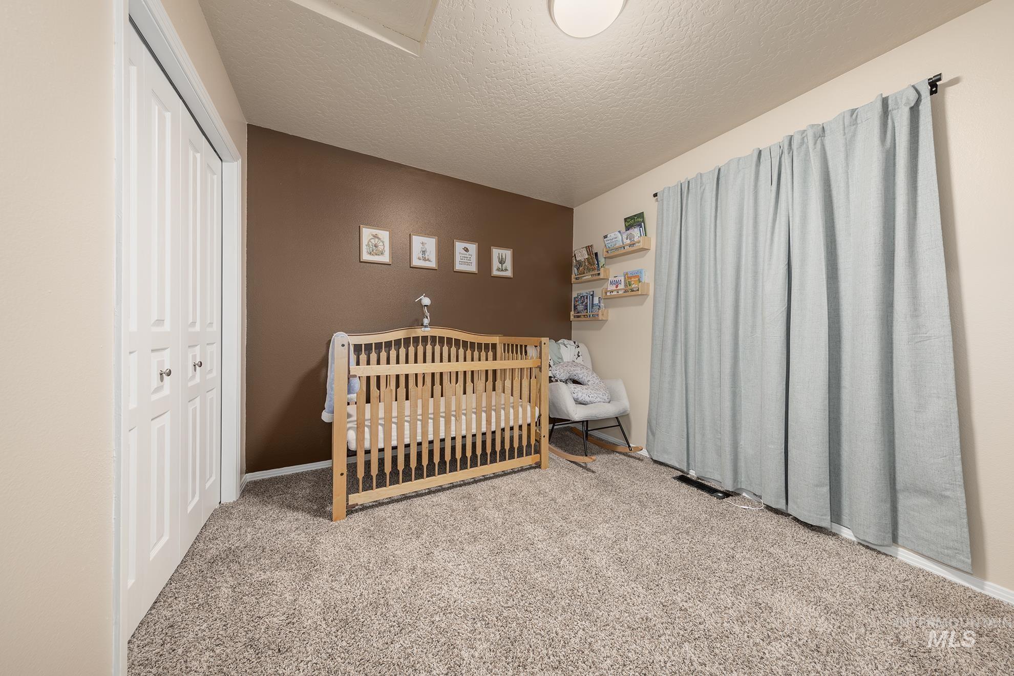 Carpeted bedroom featuring a crib, a textured ceiling, and a closet