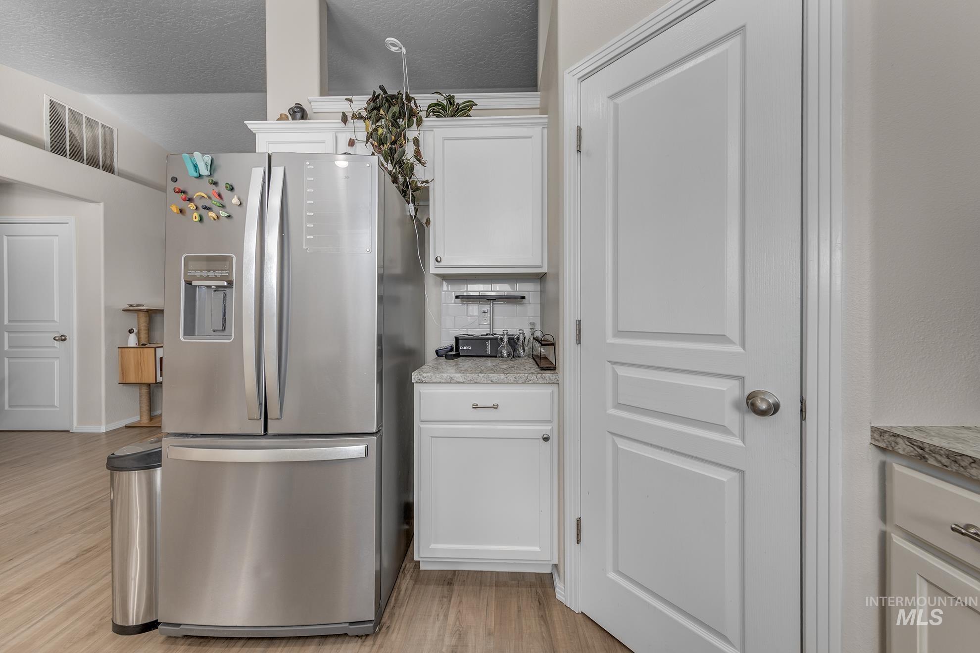 Kitchen with white cabinetry, stainless steel fridge with ice dispenser, backsplash, light countertops, and a textured ceiling