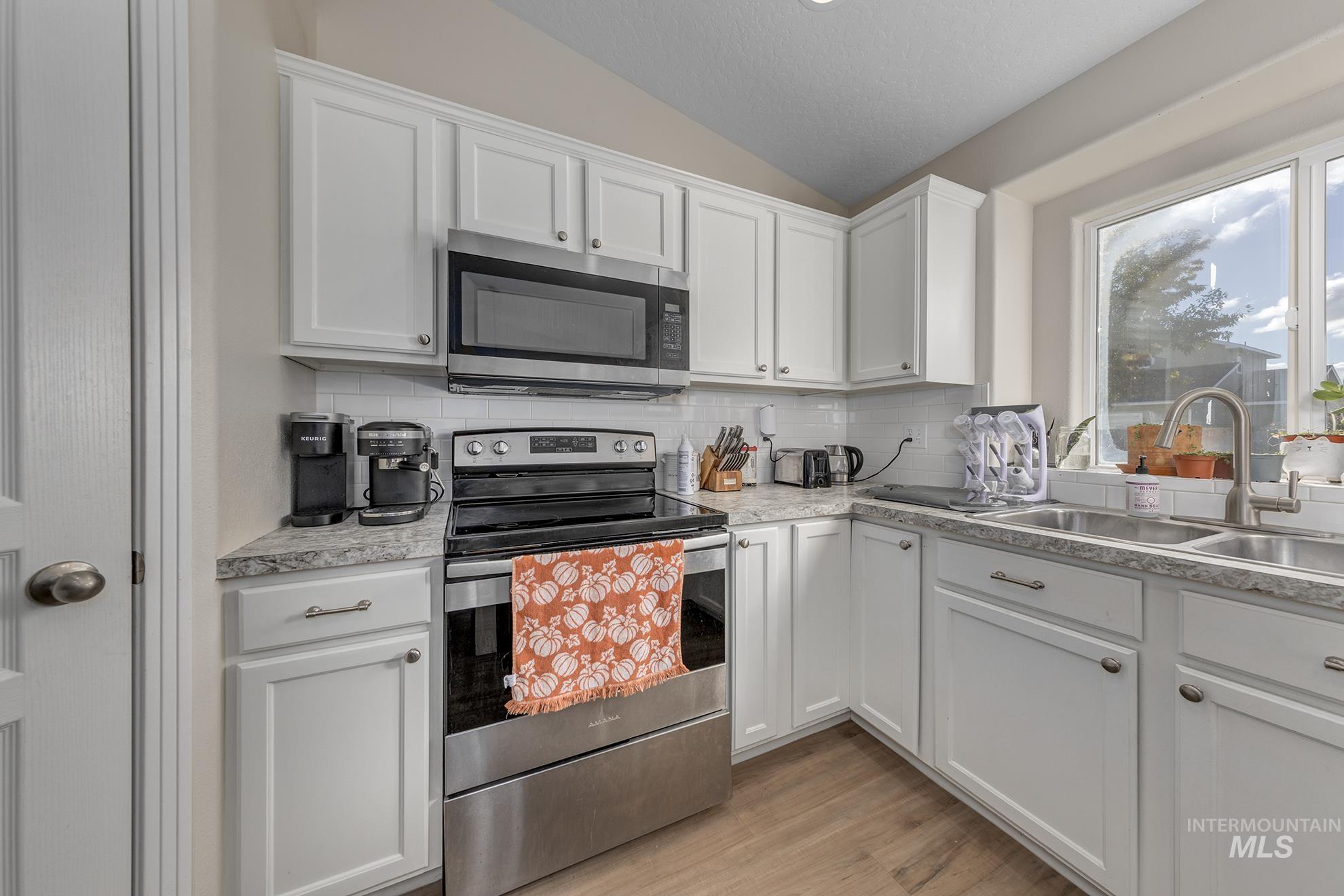 Kitchen featuring appliances with stainless steel finishes, lofted ceiling, white cabinets, light countertops, and backsplash