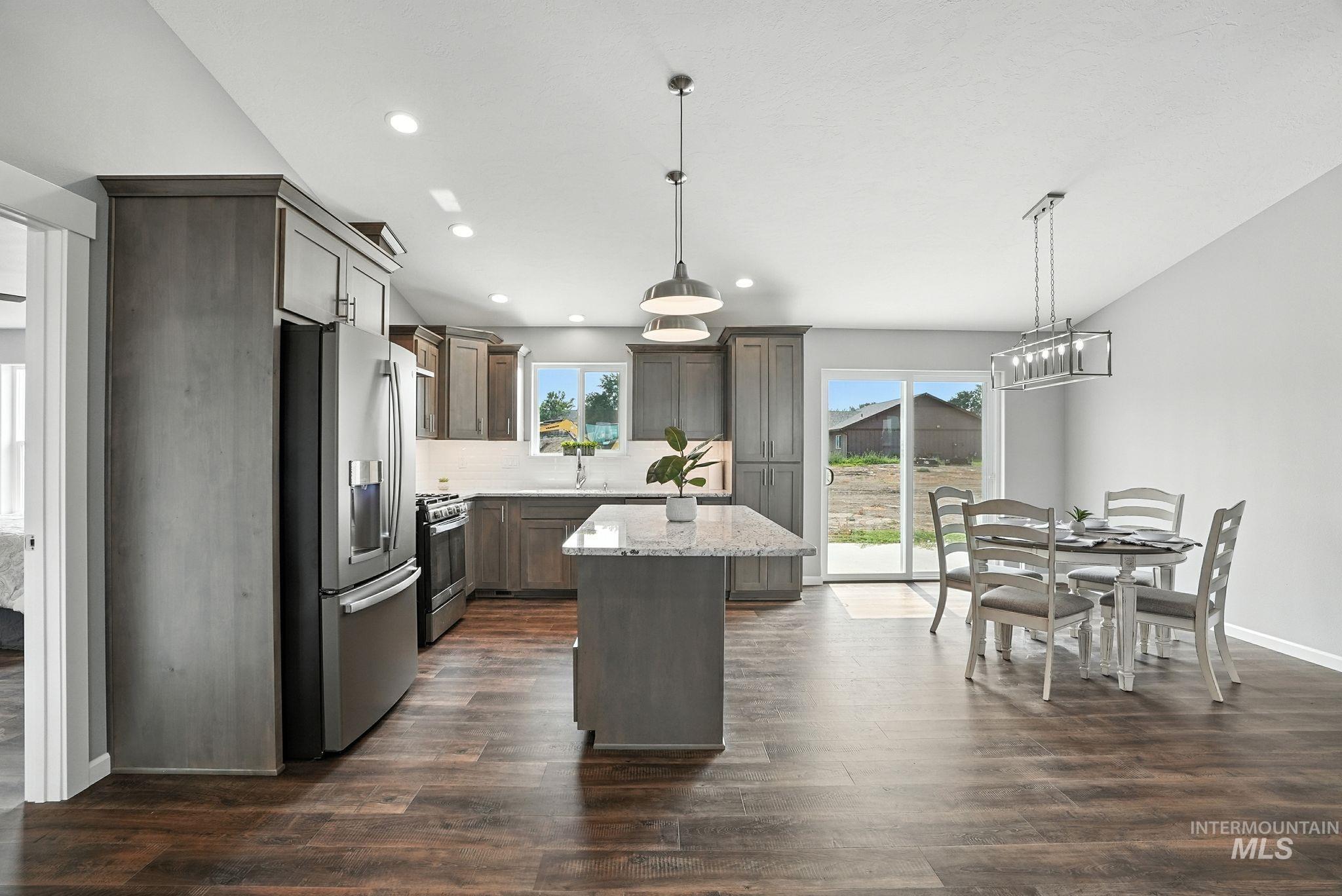 Kitchen with appliances with stainless steel finishes, decorative light fixtures, a kitchen island, light stone counters, and recessed lighting