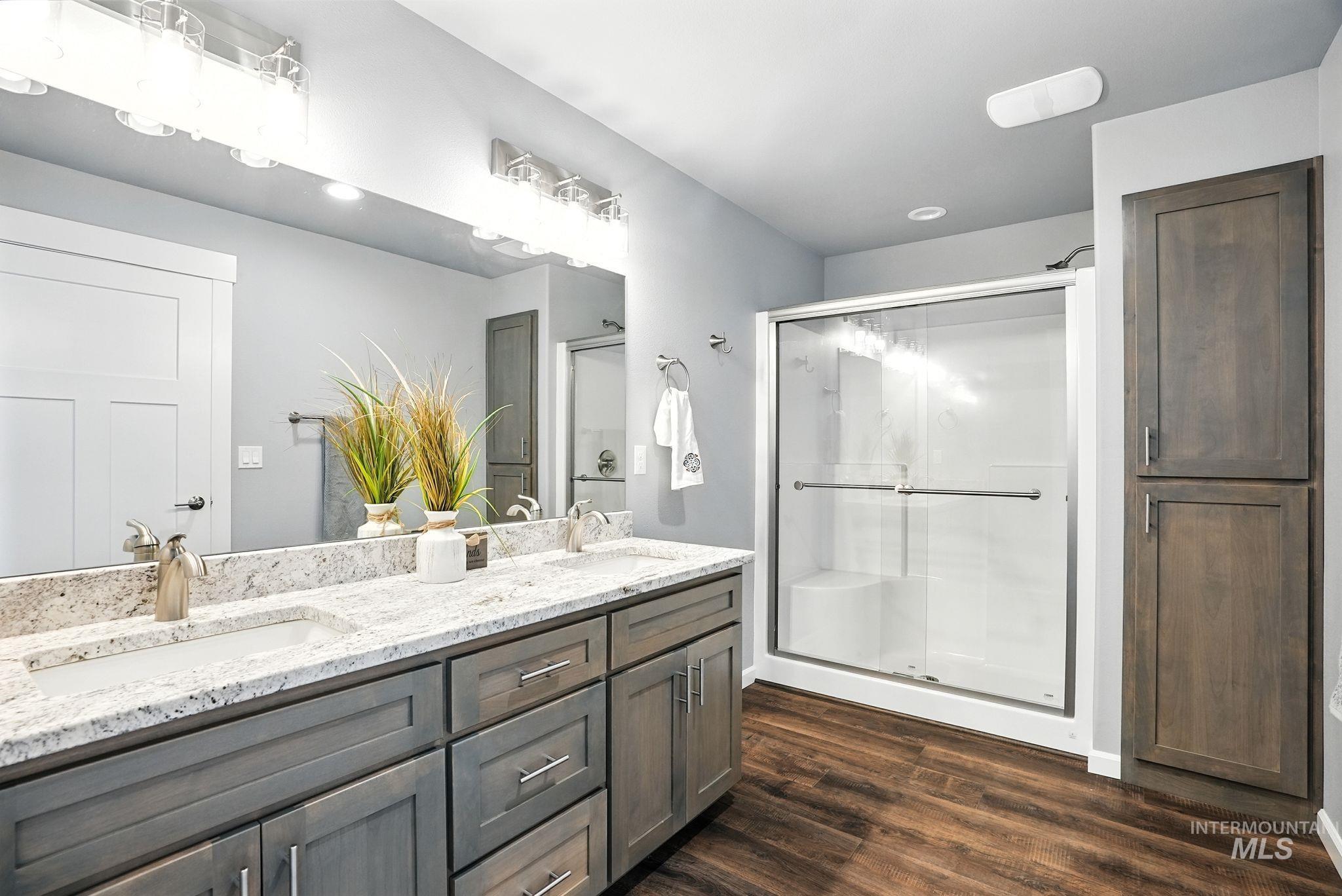 Full bath with double vanity, a shower stall, dark wood-style flooring, and recessed lighting
