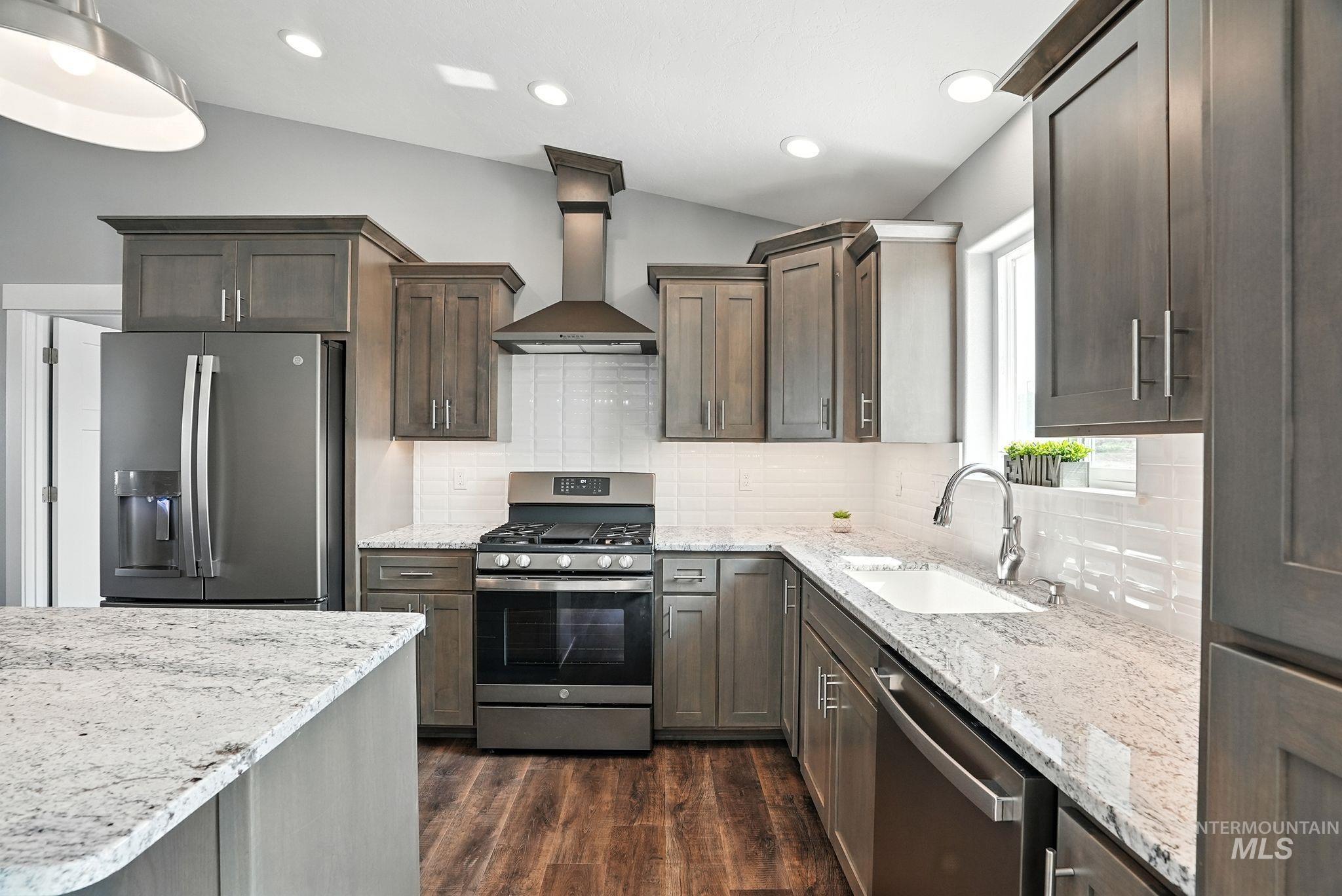 Kitchen featuring stainless steel appliances, light stone countertops, wall chimney exhaust hood, backsplash, and dark wood-type flooring