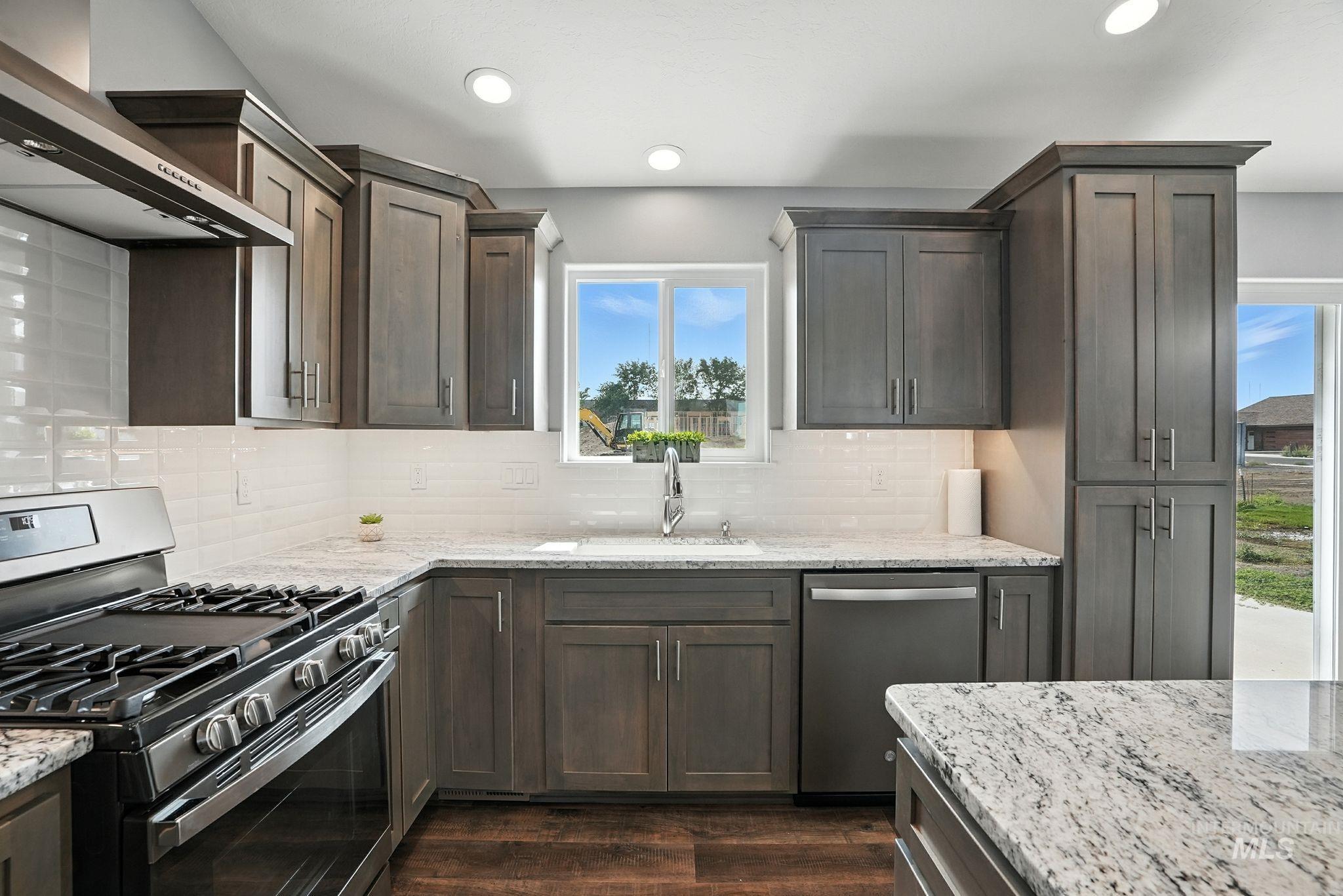 Kitchen with appliances with stainless steel finishes, wall chimney range hood, light stone countertops, dark wood-type flooring, and decorative backsplash