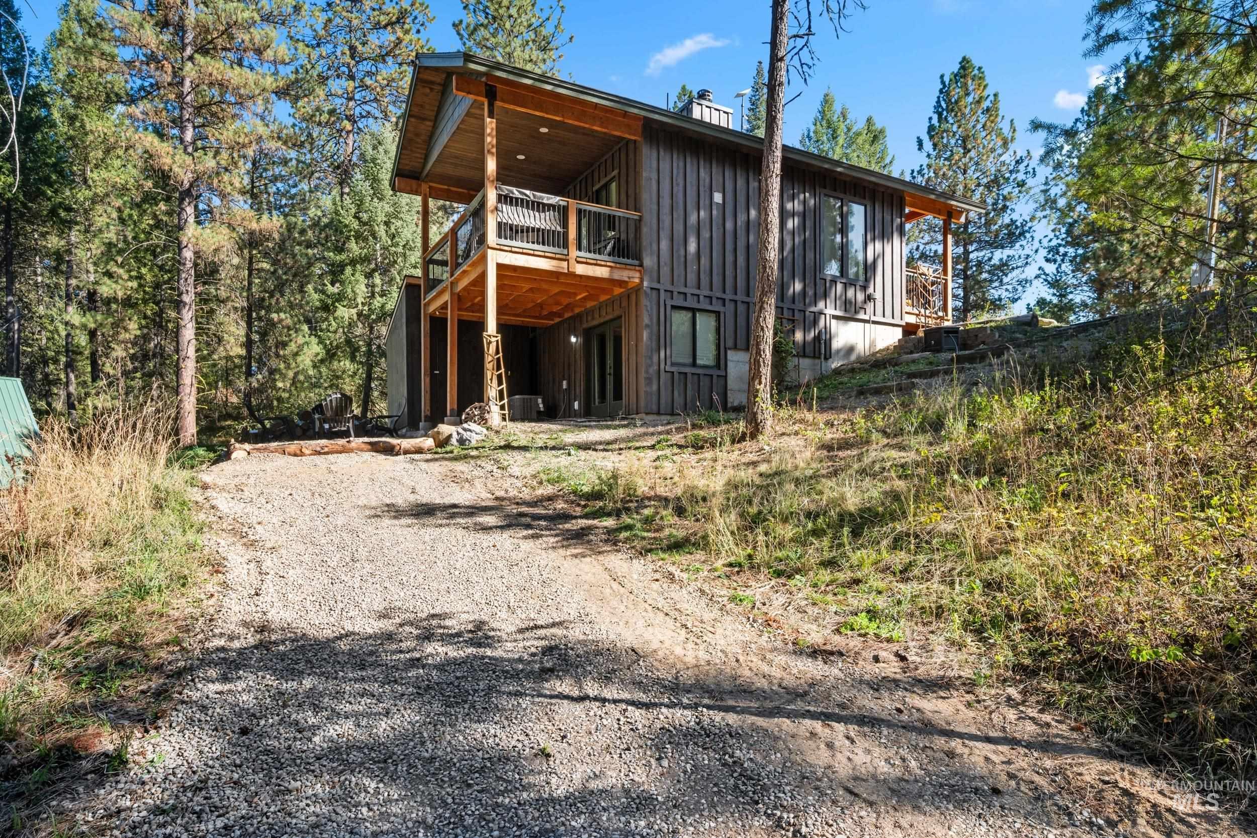 Rear view of house featuring board and batten siding, a wooden deck, driveway, and a patio area