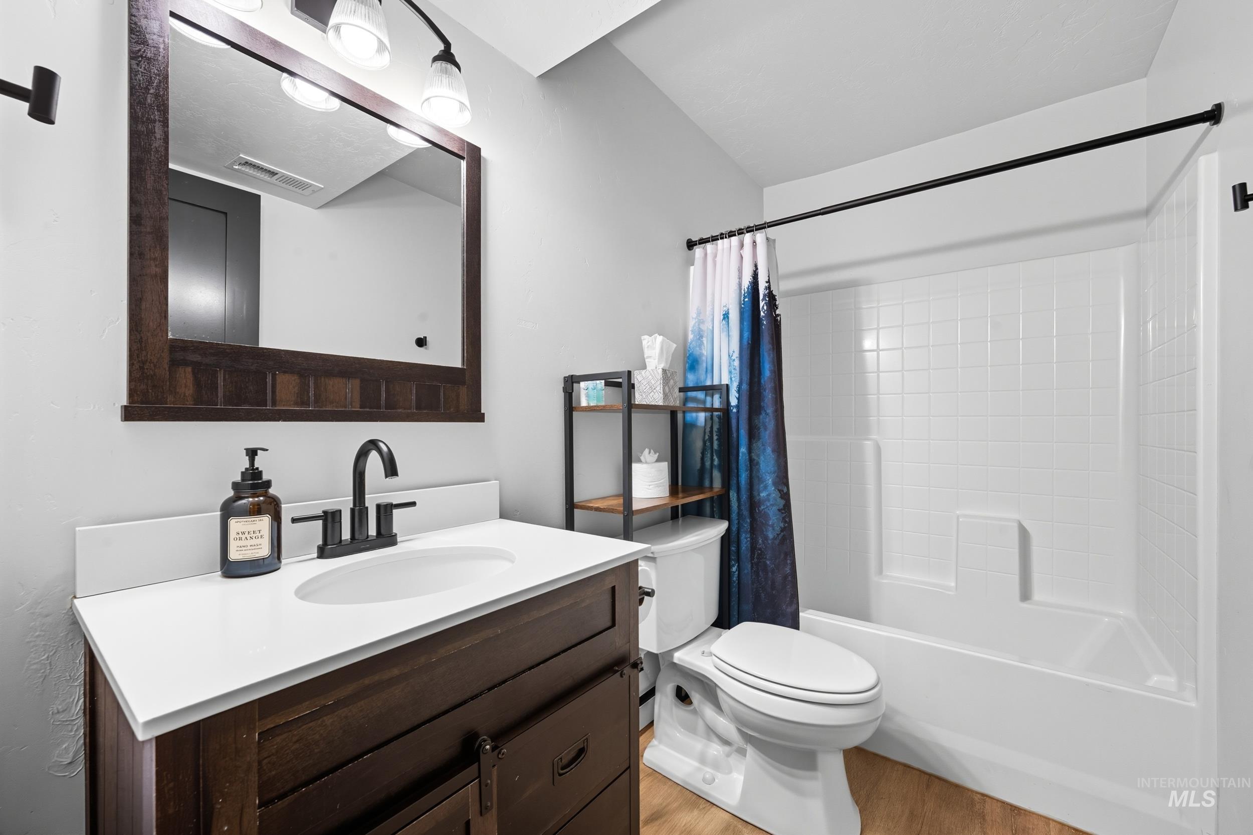 Bathroom with shower / bathtub combination with curtain, light wood-style flooring, and vanity