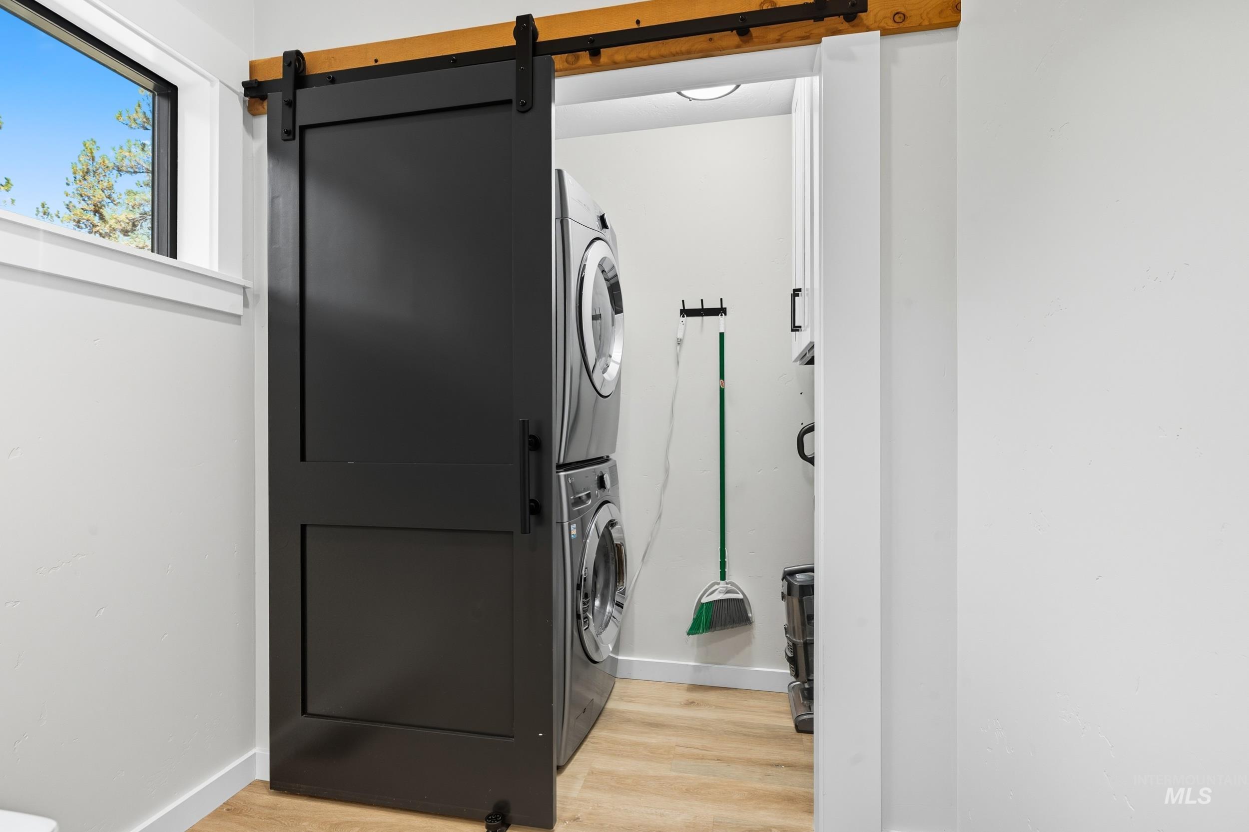 Washroom with light wood-style floors, a barn door, and stacked washer / dryer