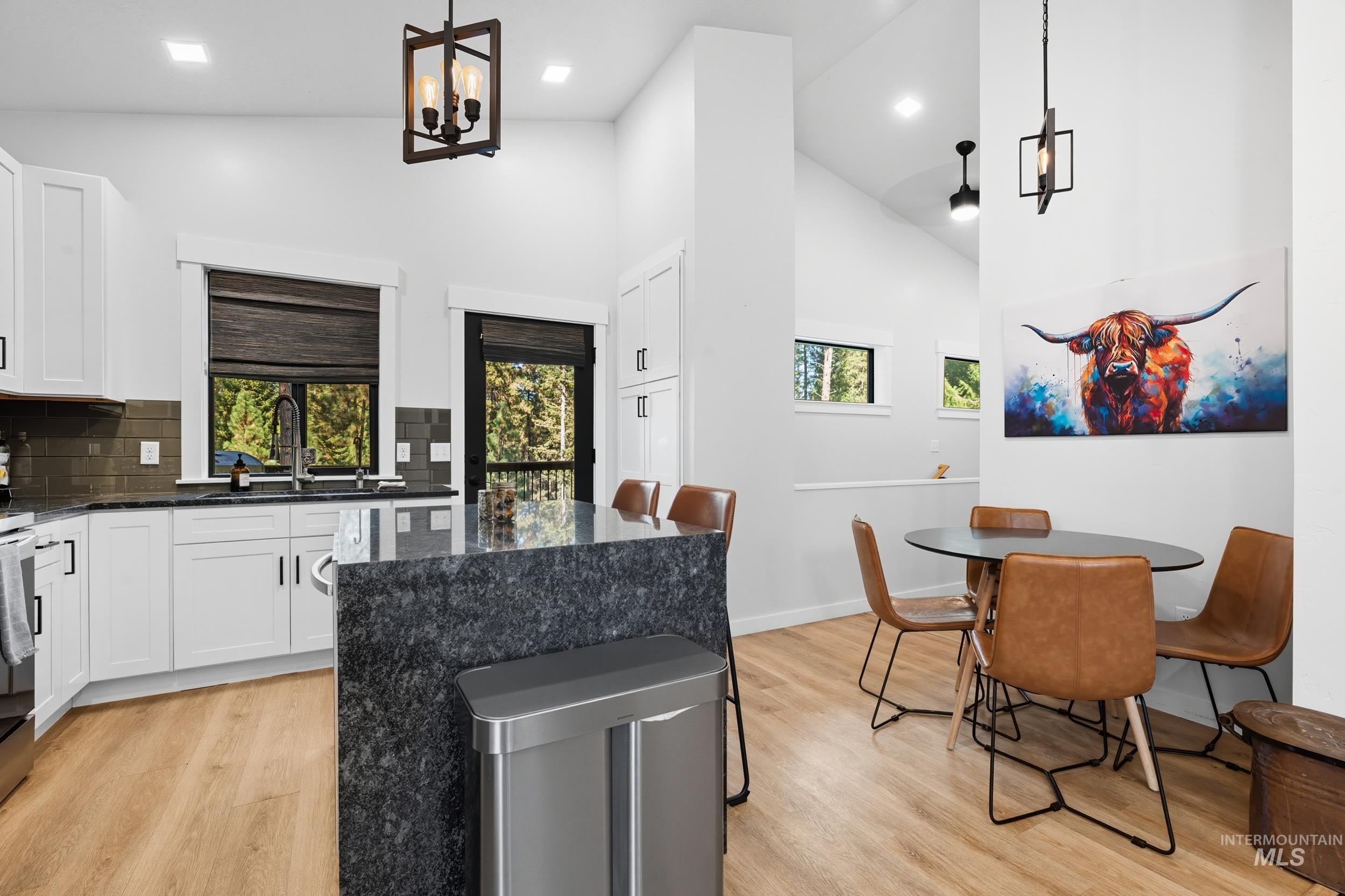 Kitchen featuring dark stone counters, plenty of natural light, decorative backsplash, high vaulted ceiling, and light wood-type flooring