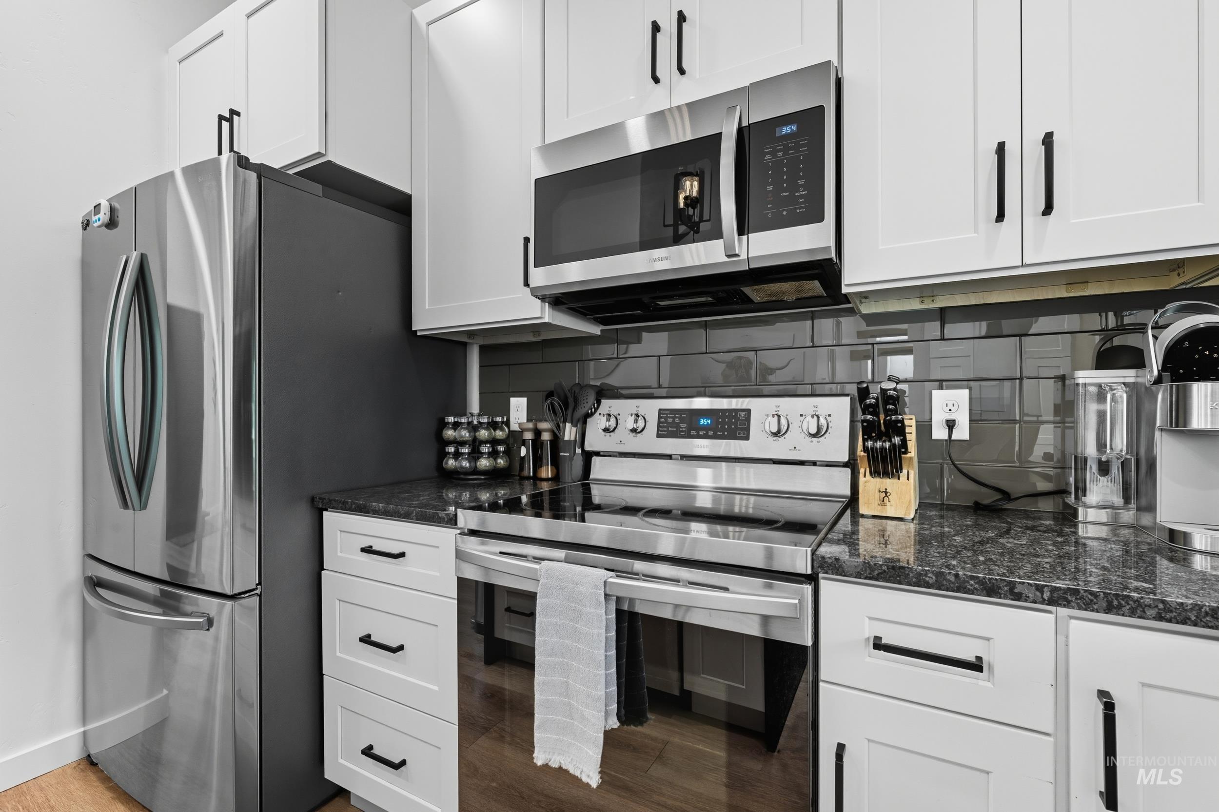 Kitchen featuring stainless steel appliances, backsplash, white cabinets, and dark stone counters