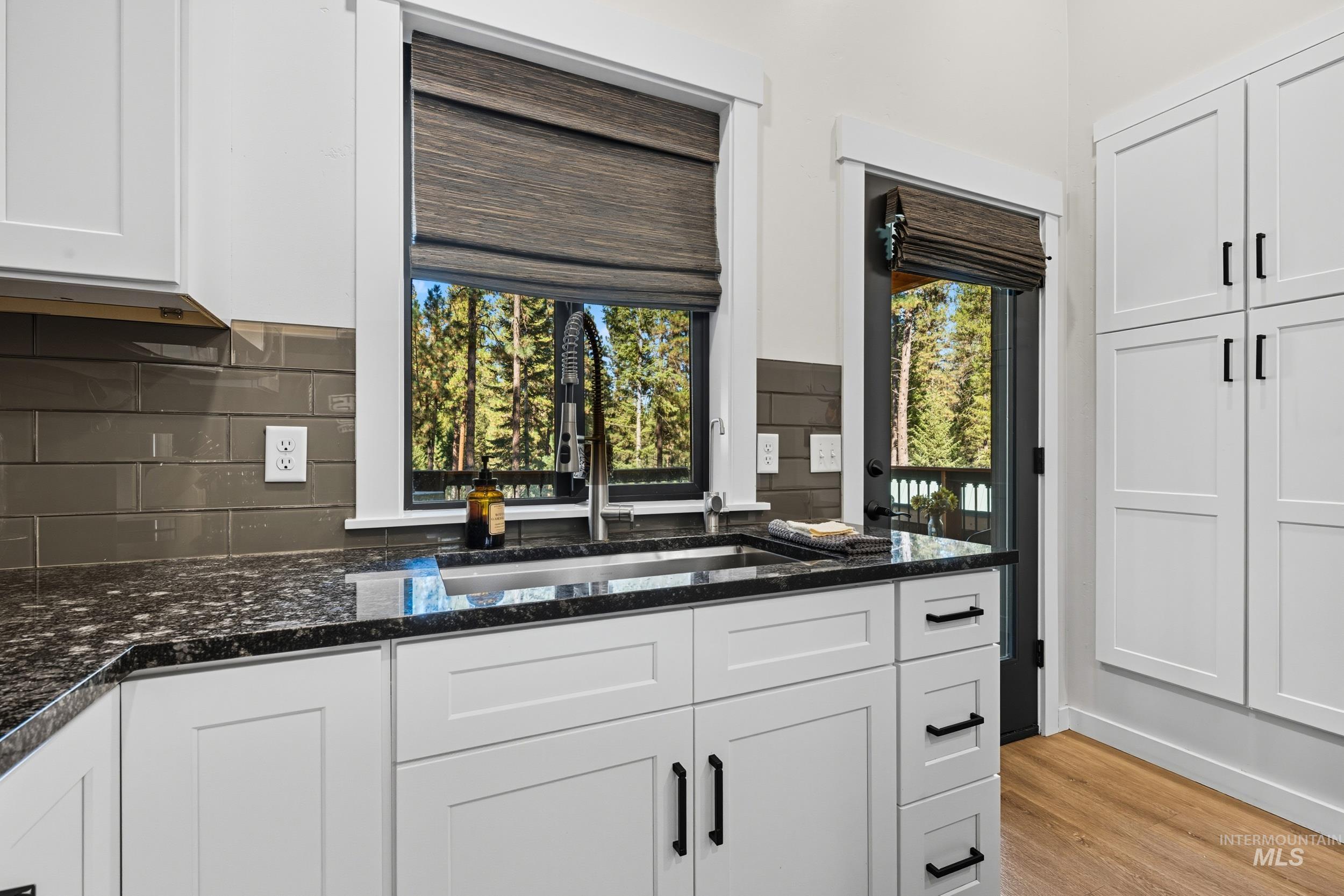 Kitchen with dark stone counters, white cabinets, backsplash, and light wood finished floors