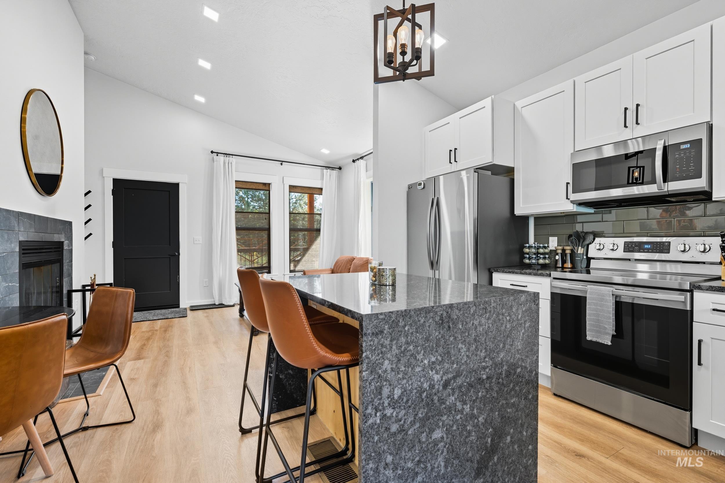 Kitchen featuring stainless steel appliances, backsplash, a kitchen bar, dark stone counters, and recessed lighting