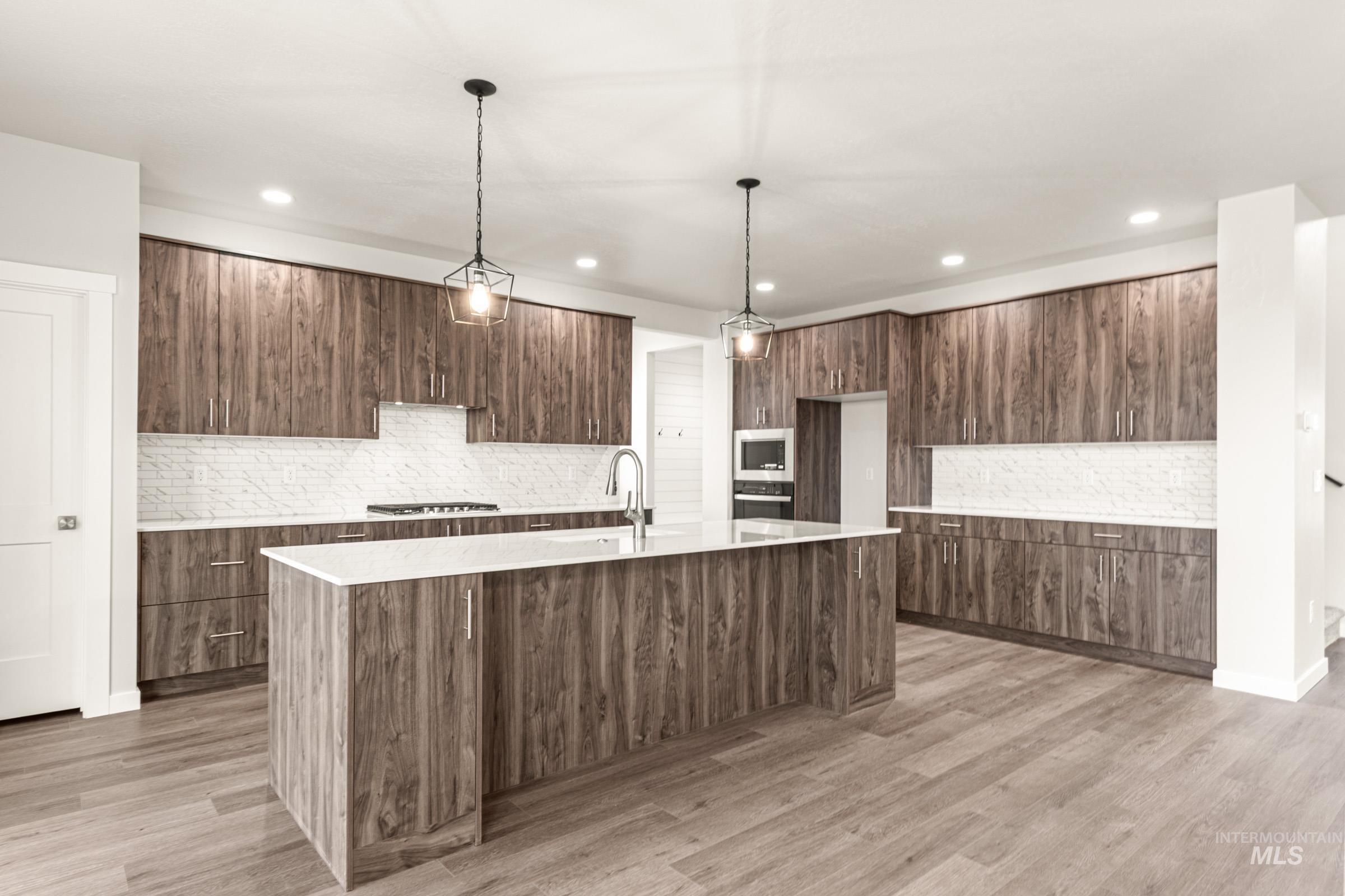 Contemporary kitchen featuring a central island with a sink, extensive wood-finish cabinetry, white countertops, and a white subway tile backsplash