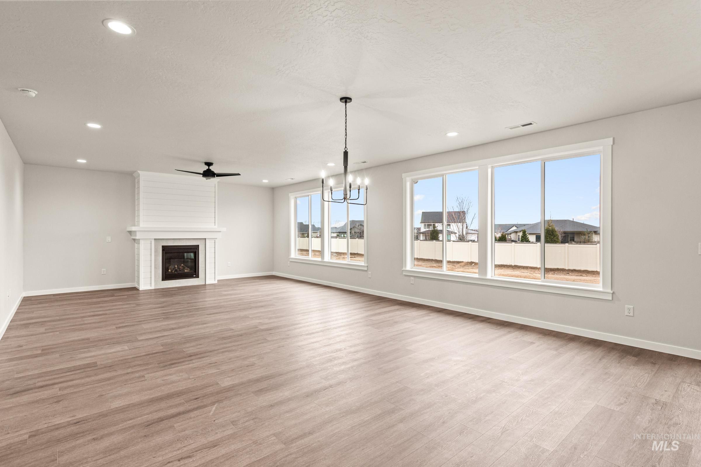 Spacious room featuring wood-finish flooring, a white shiplap fireplace with mantel, and multiple large windows