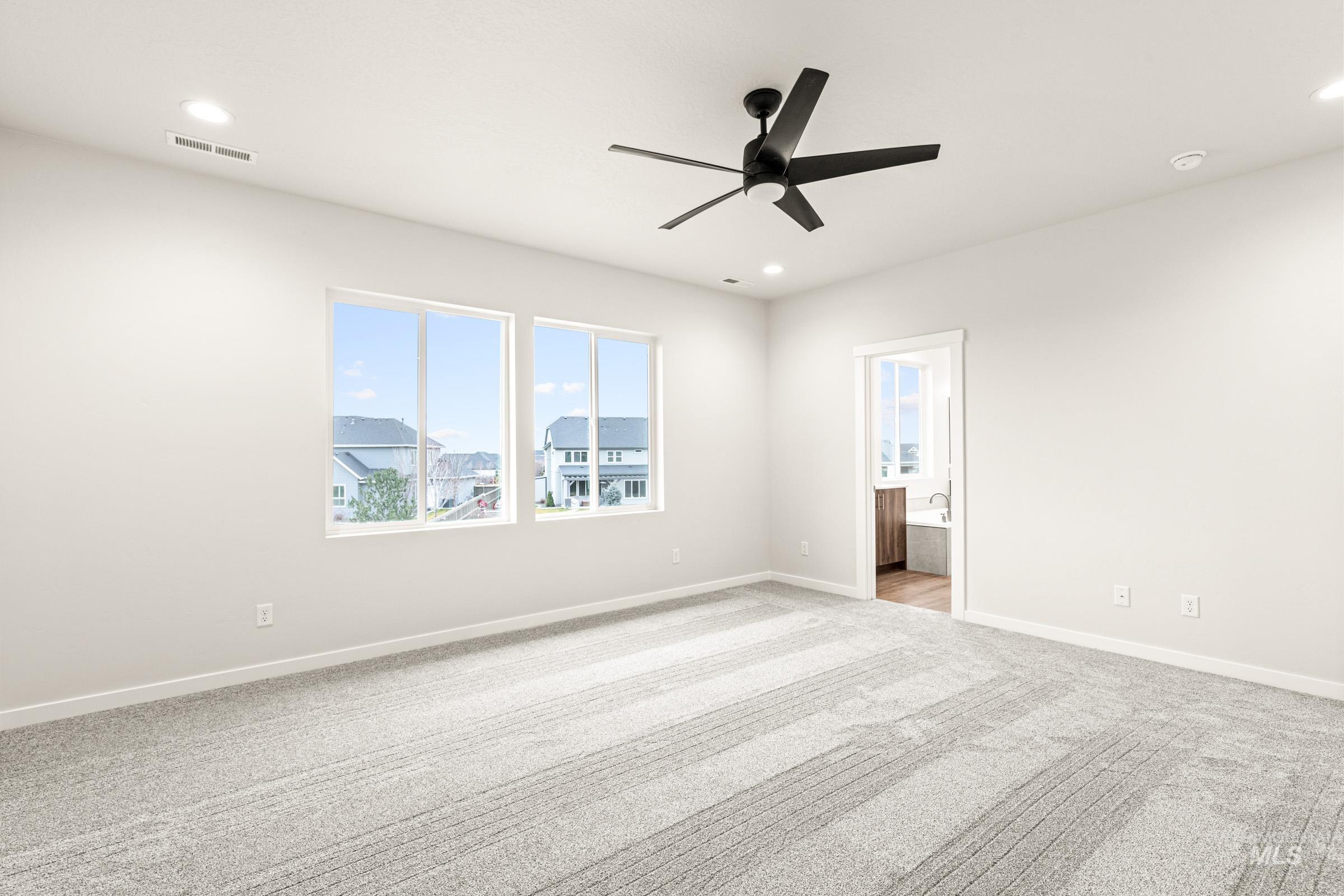 Spacious room featuring light gray carpeting, a contemporary black ceiling fan, recessed lighting, and two large windows