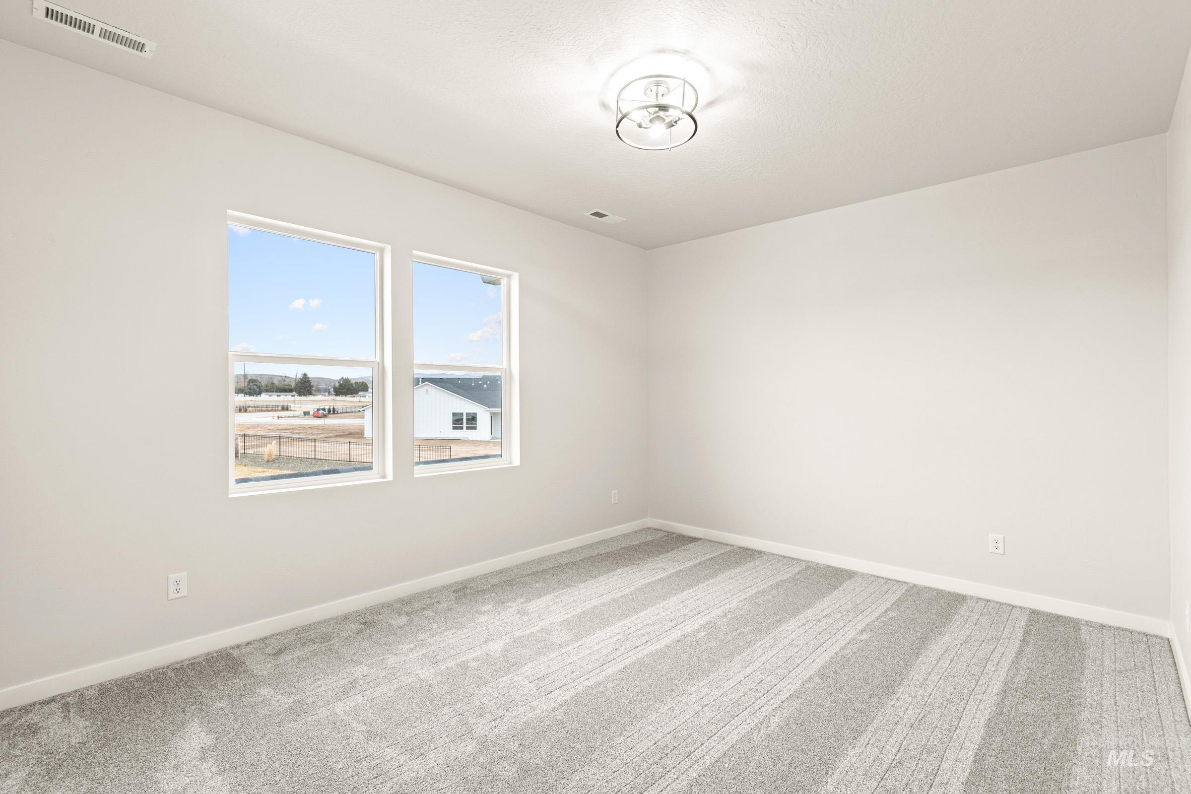 Spacious room featuring two large windows, neutral wall tones, patterned gray carpeting, white baseboards, and a contemporary ceiling light fixture