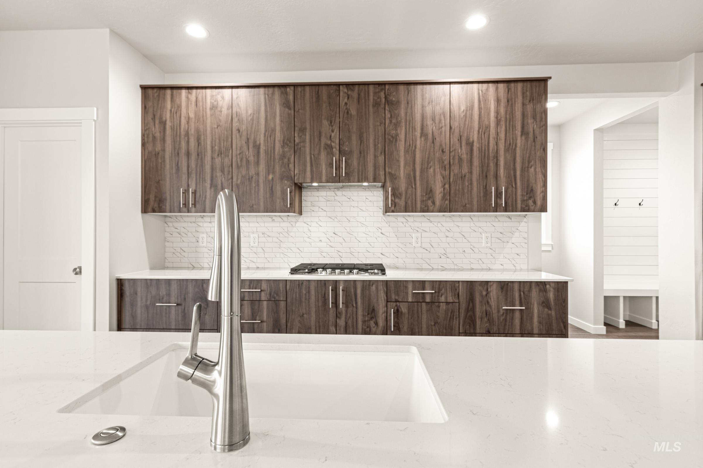 Contemporary kitchen featuring white solid surface countertops, wood-finish cabinetry, a gas cooktop, and a white subway tile backsplash