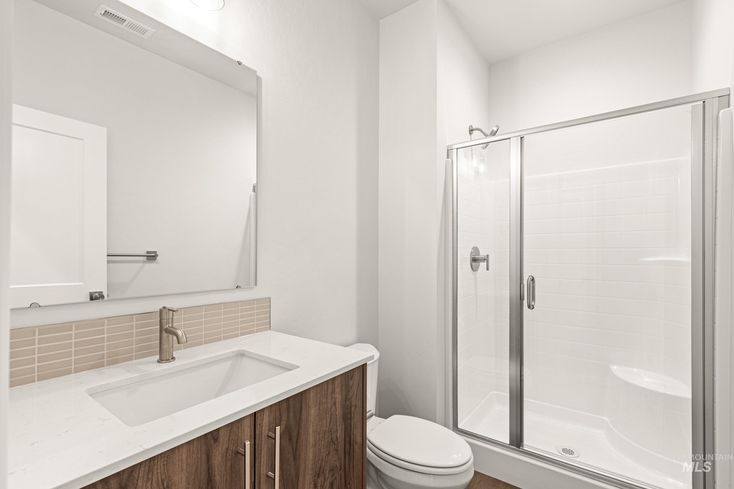 Bathroom featuring a wood-finish vanity with an integrated sink, a large wall mirror, and a glass-enclosed shower with a built-in bench