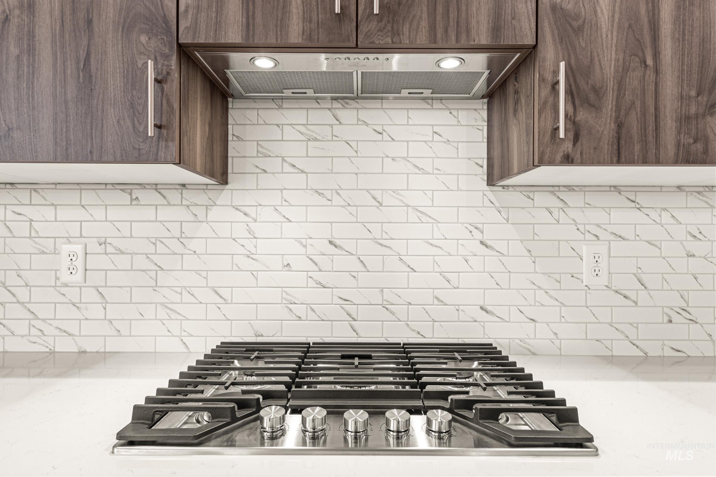 Integrated stainless steel gas range with a coordinating vent hood, set against a white subway tile backsplash with subtle veining