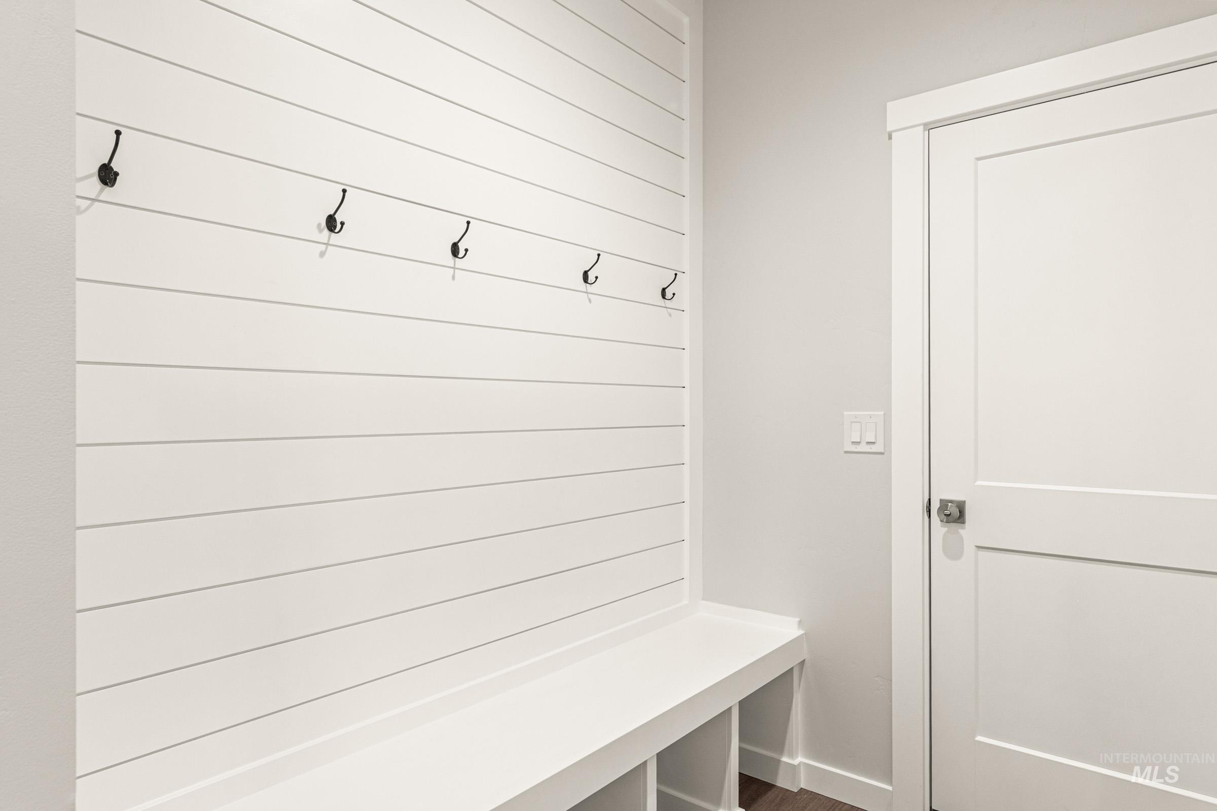 Built-in shiplap mudroom bench with cubby storage, featuring coat hooks and white interior door with contemporary hardware