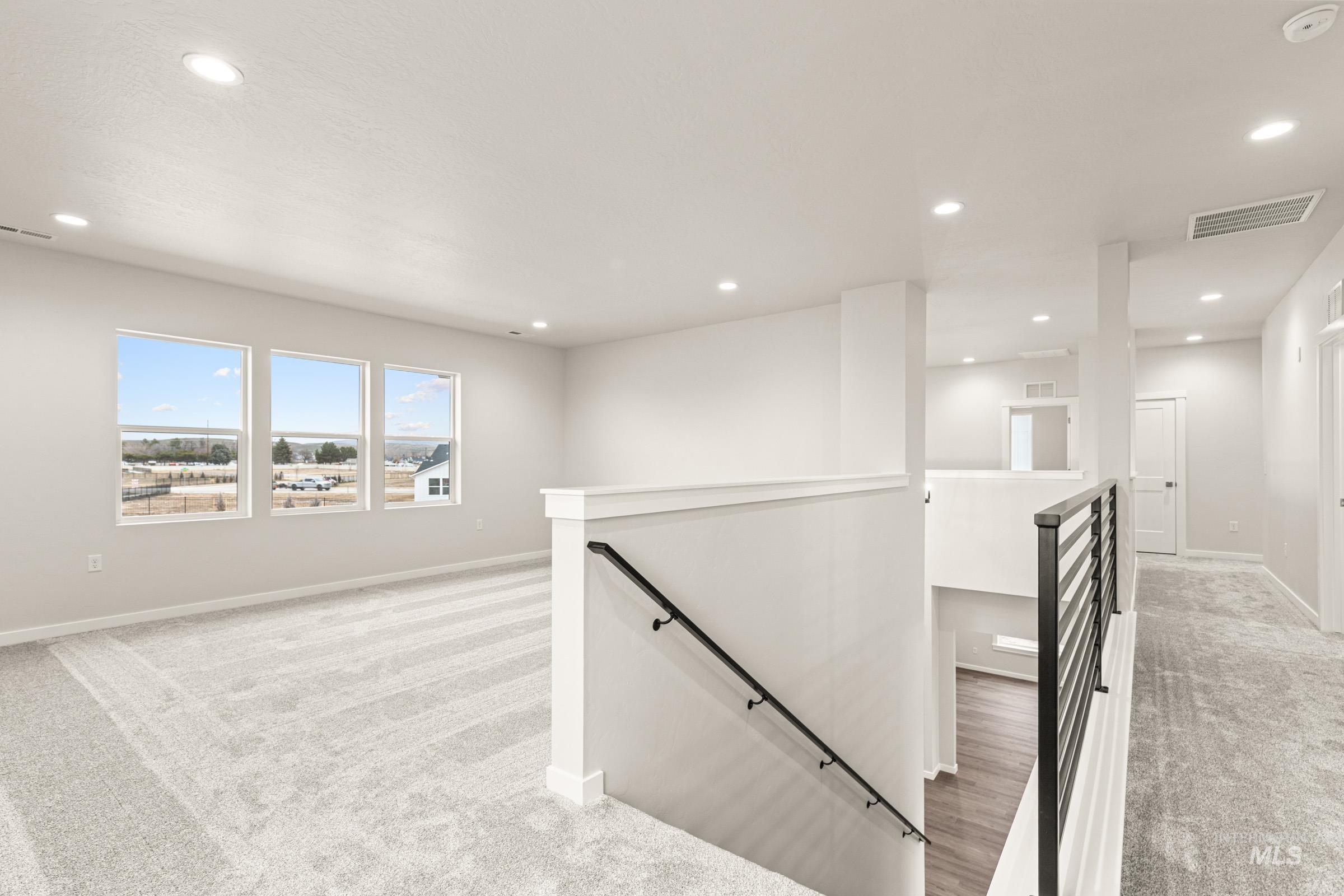 Bright upper-level common area featuring three large windows, recessed lighting, neutral carpeting, and a contemporary metal stair railing