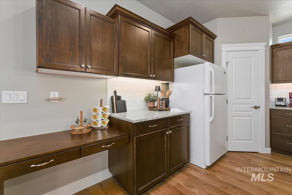 Kitchen workstation featuring a built-in desk with two drawers, dark wood-finish cabinetry, light granite-style countertops, and a white subway tile backsplash