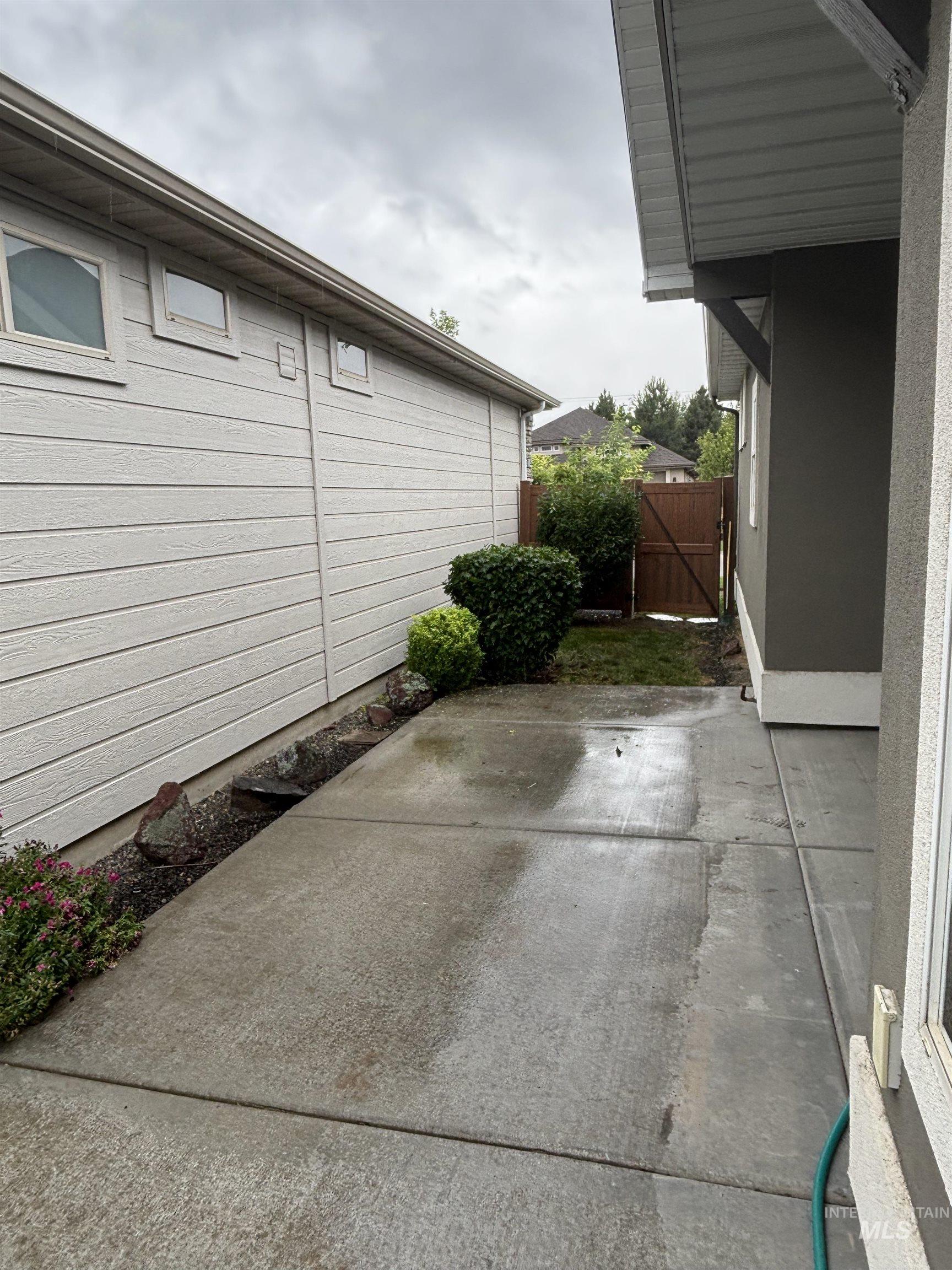 Concrete walkway featuring horizontal siding, mature shrubs, and a wood privacy fence