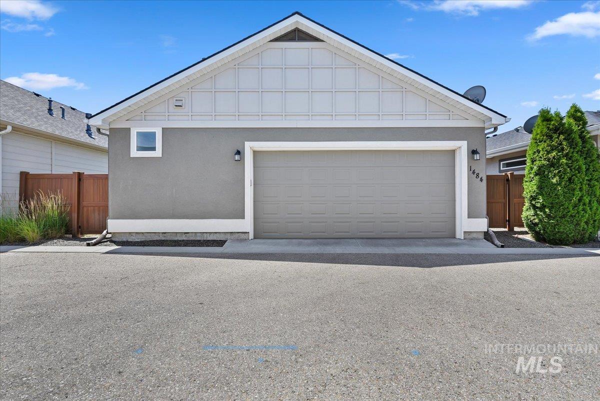 Attached garage with a neutral-toned door, stucco exterior, white trim, and a gabled roofline