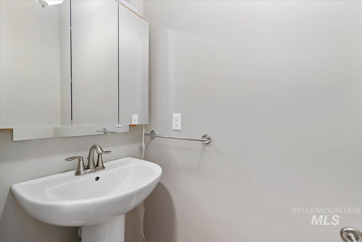 Pedestal sink with a brushed nickel faucet, complemented by a mirrored medicine cabinet and a wall-mounted towel bar