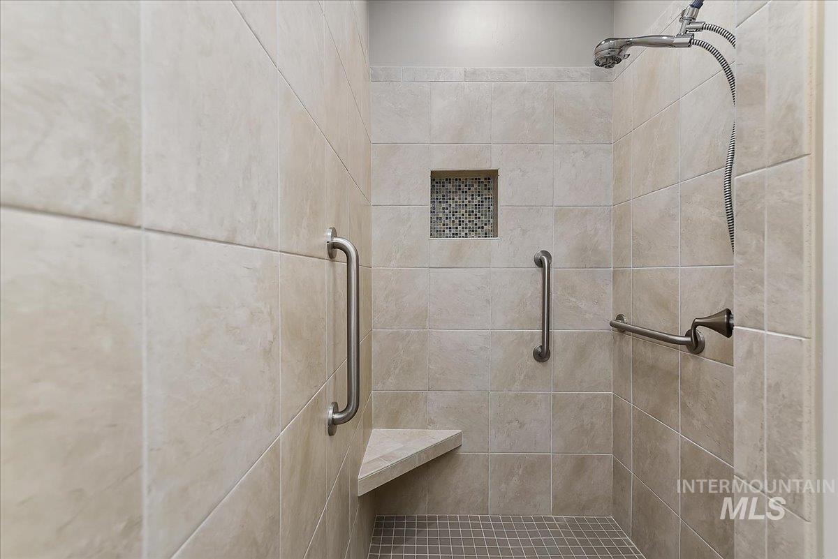 Tiled walk-in shower featuring a built-in bench, recessed shelf with mosaic tile accent, multiple grab bars, and a handheld showerhead
