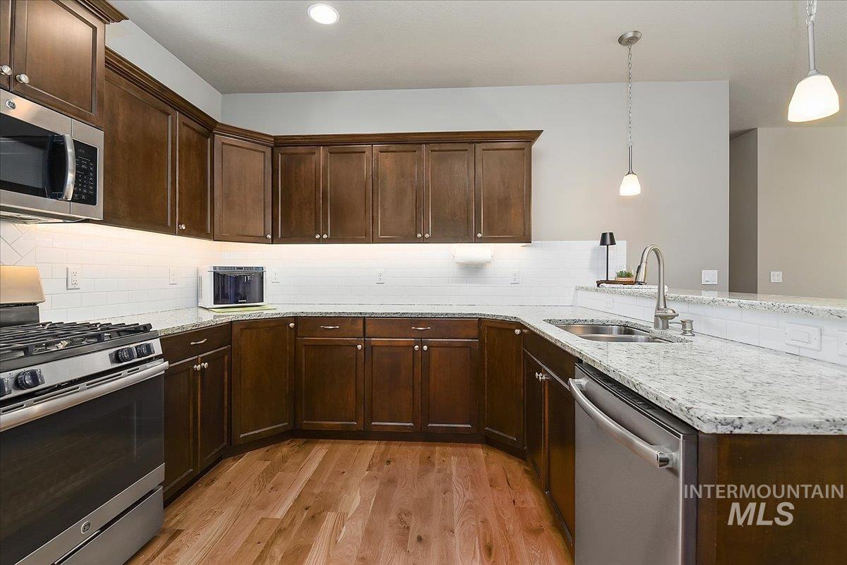 Kitchen featuring wood-finish flooring, dark wood cabinetry, granite-style countertops, and a subway tile backsplash