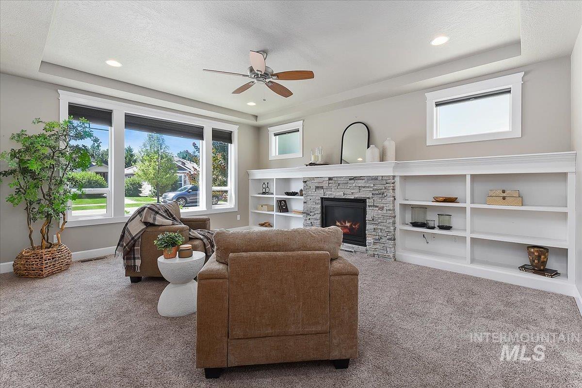 Living area featuring a stone-clad fireplace, integrated white built-in shelving, plush carpeting, and recessed lighting