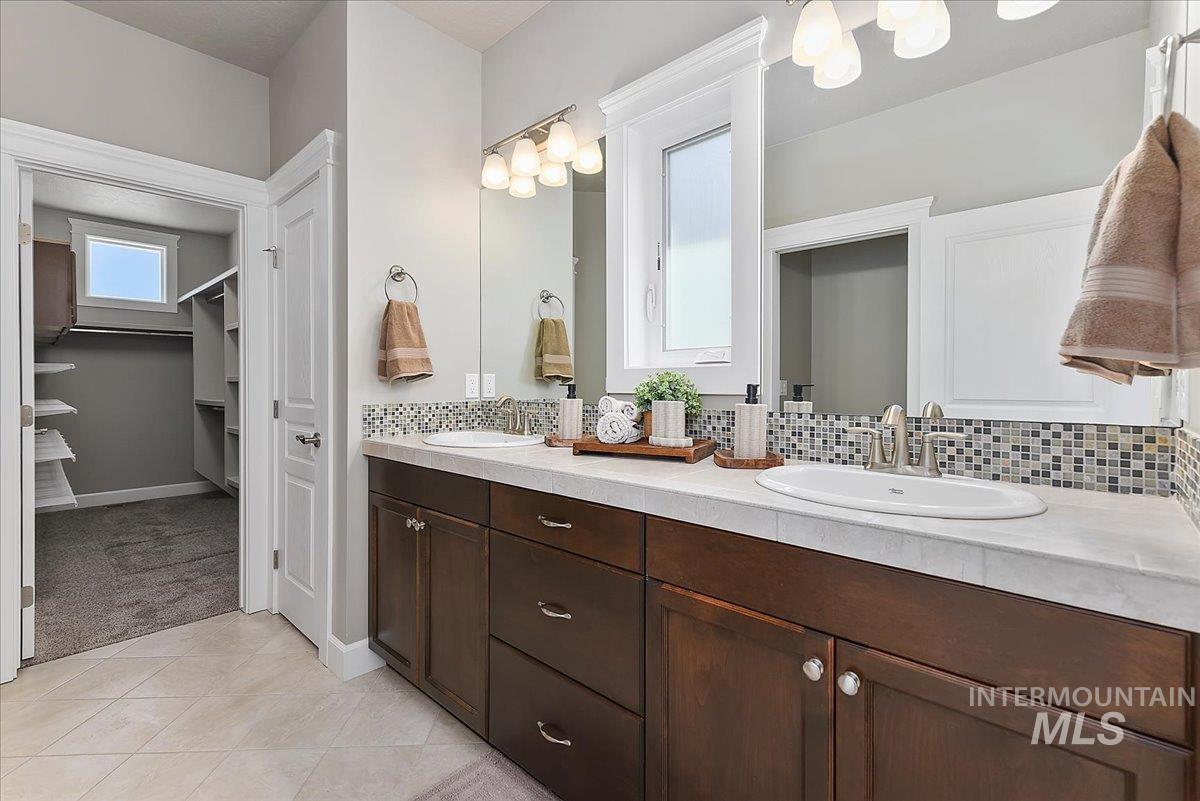 Bathroom featuring a dual vanity with dark wood cabinetry, light-toned countertops, and mosaic tile backsplash