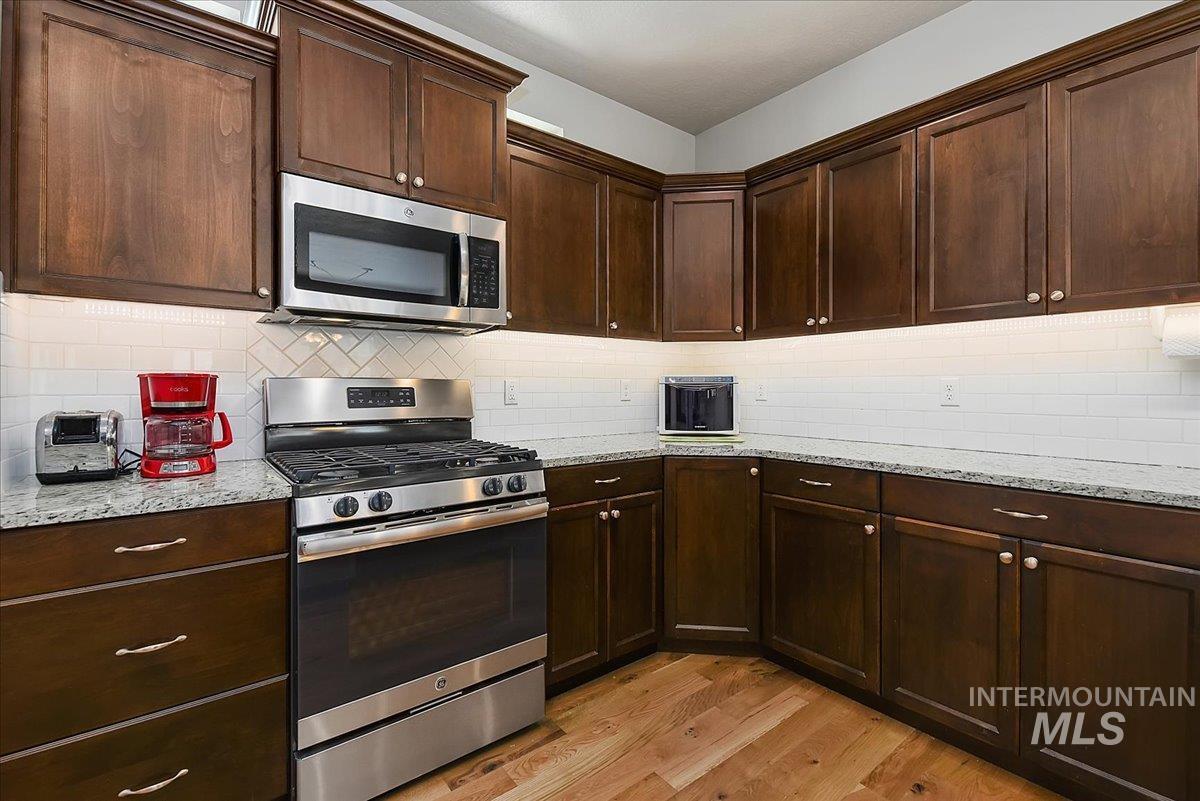 Kitchen featuring dark wood cabinetry, stainless steel appliances, granite countertops, white subway tile backsplash, and wood-finish flooring