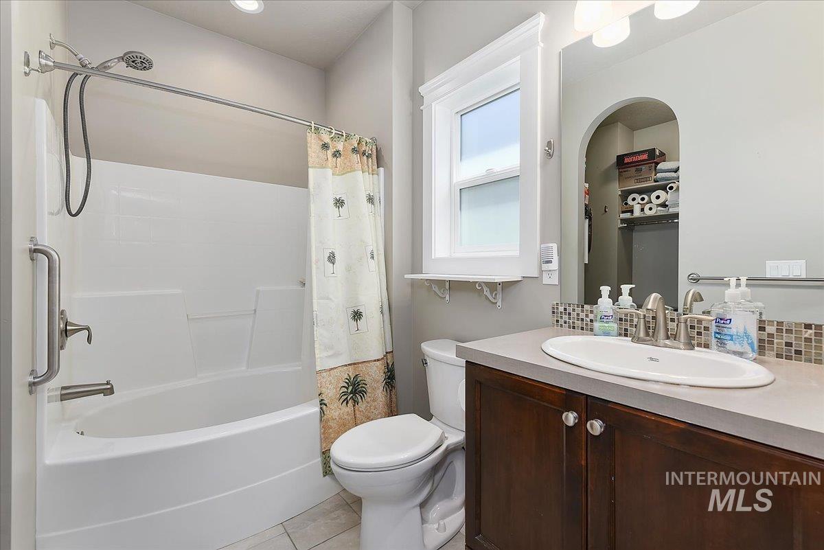 Bathroom featuring a white bathtub/shower combination with grab bar, a window for natural light, a wood-finish vanity with an integrated sink, and a mosaic tile backsplash