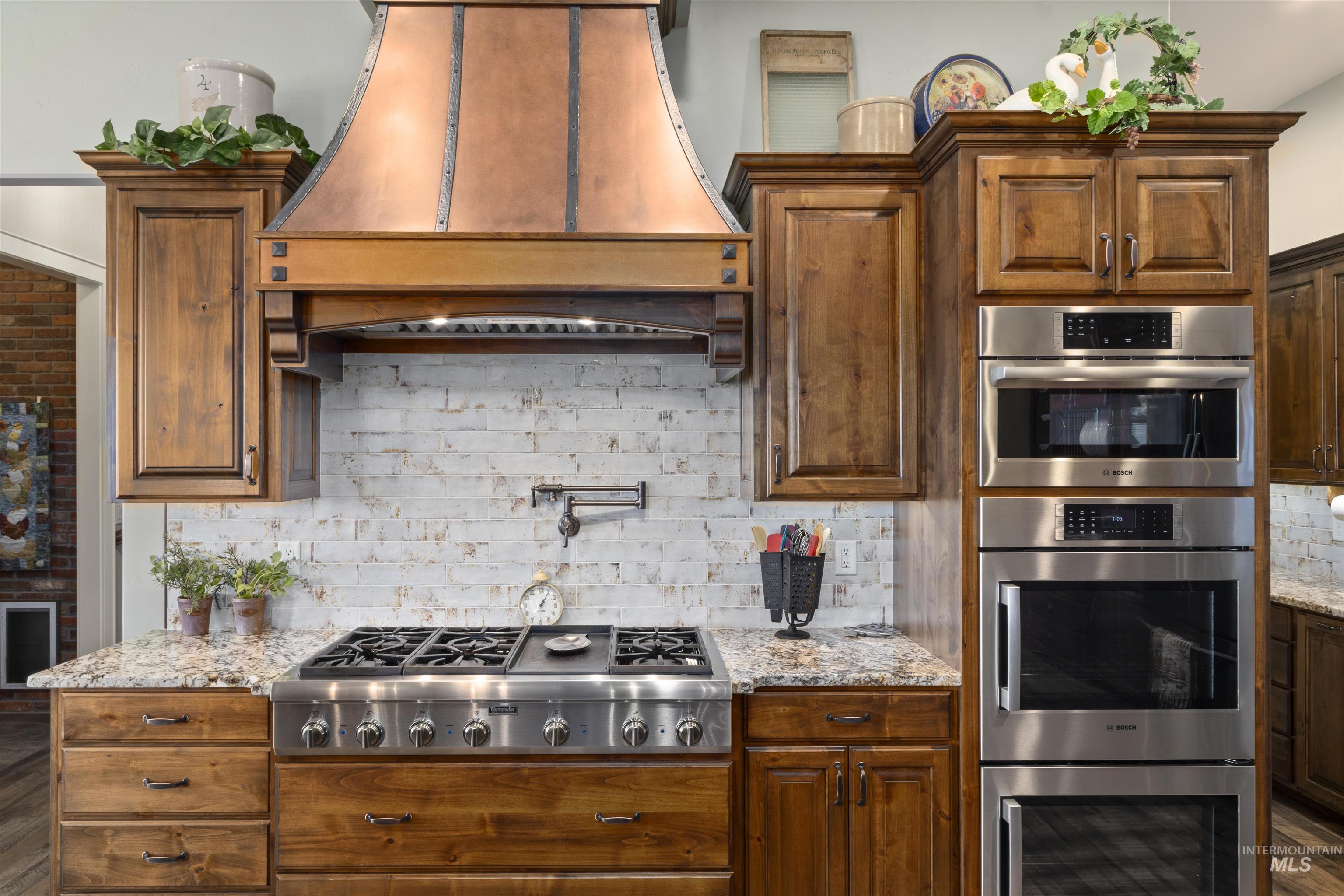 Kitchen featuring custom range hood, stainless steel appliances, tasteful backsplash, and light stone counters