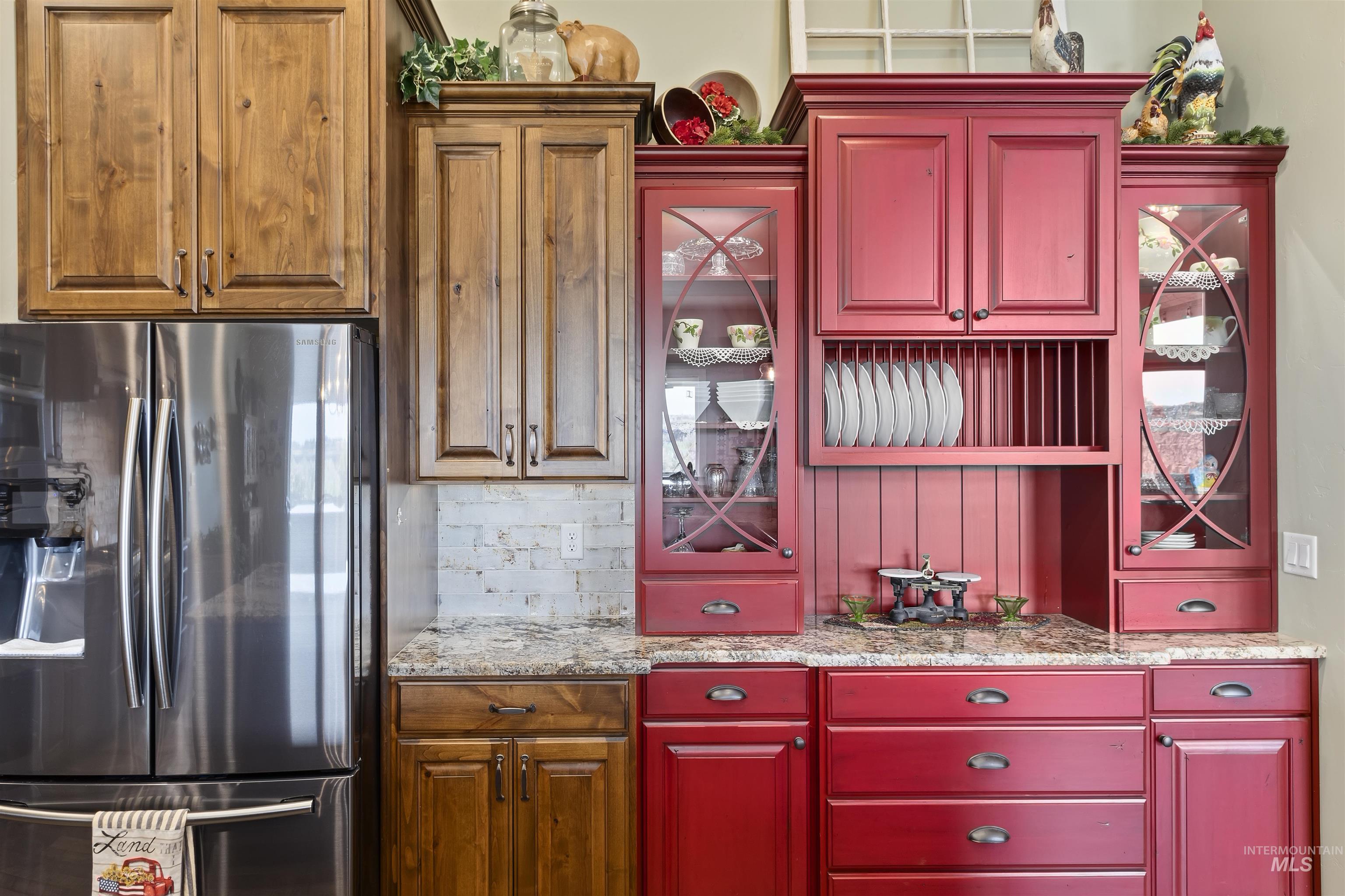 Kitchen with stainless steel fridge with ice dispenser, backsplash, light stone counters, and glass insert cabinets