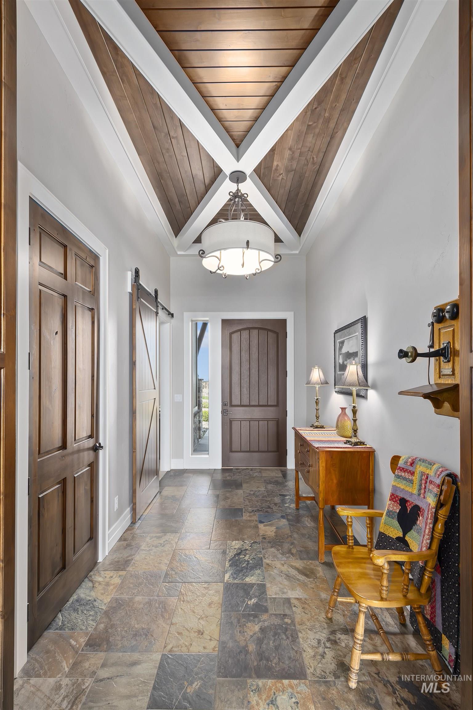 Entrance foyer with a barn door, a wooden ceiling with exposed beams, and stone tile flooring