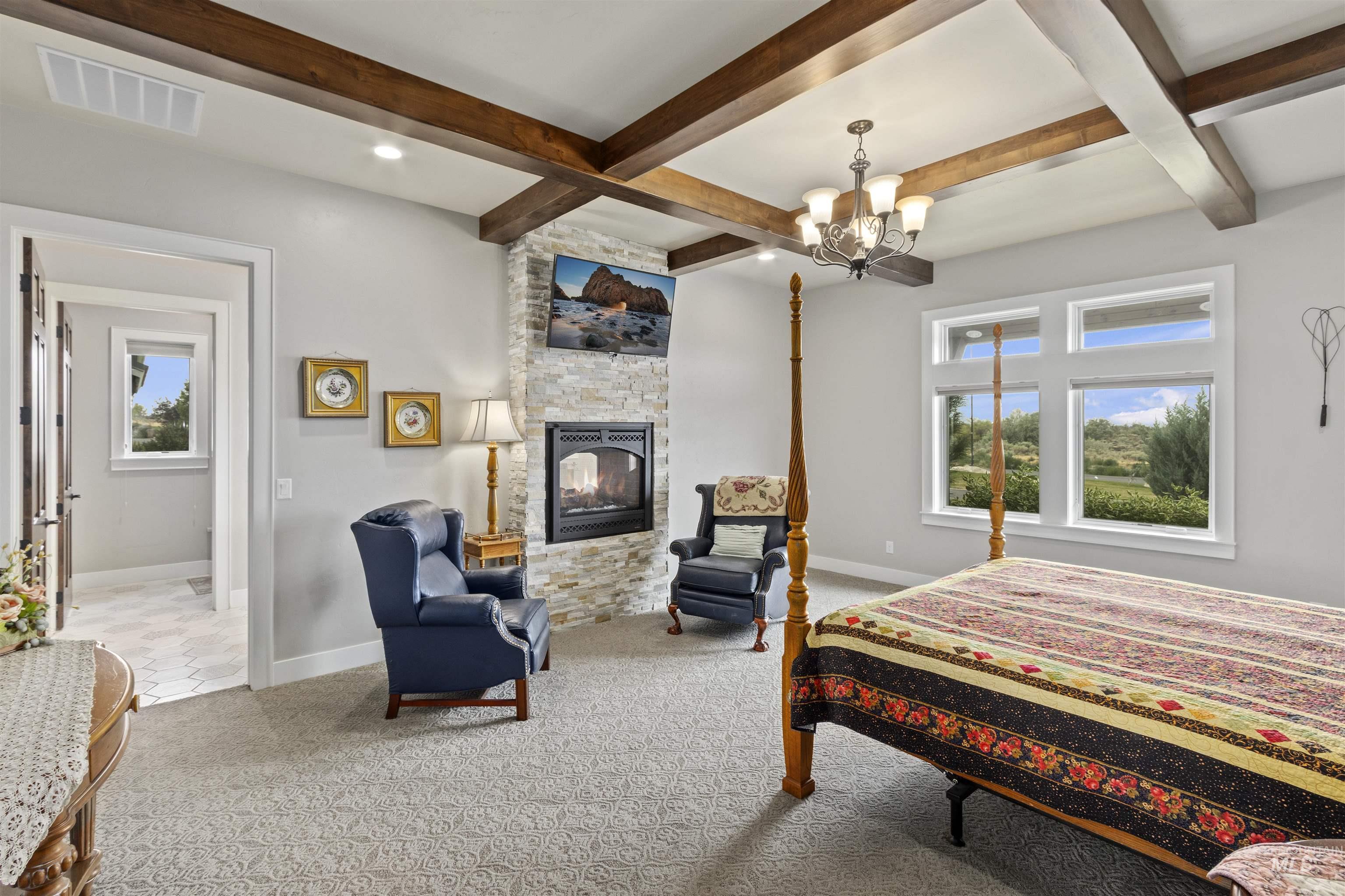 Bedroom with a stone fireplace, coffered ceiling, beamed ceiling, carpet flooring, and a chandelier