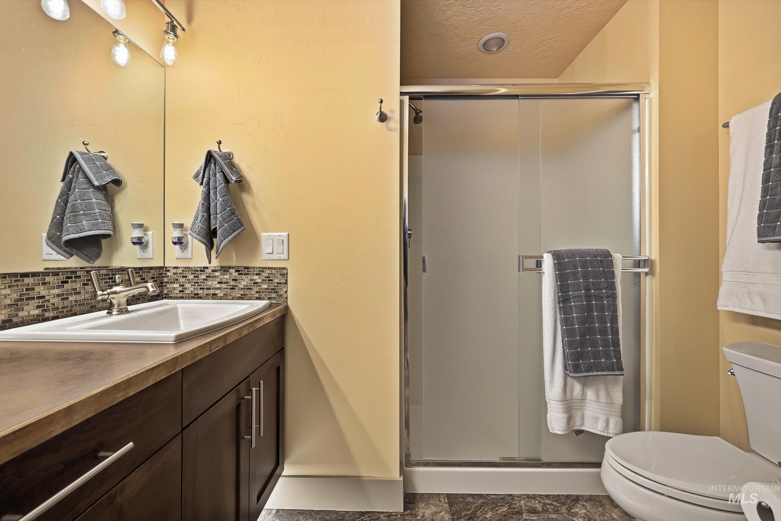Bathroom with vanity, a textured ceiling, a shower stall, and decorative backsplash