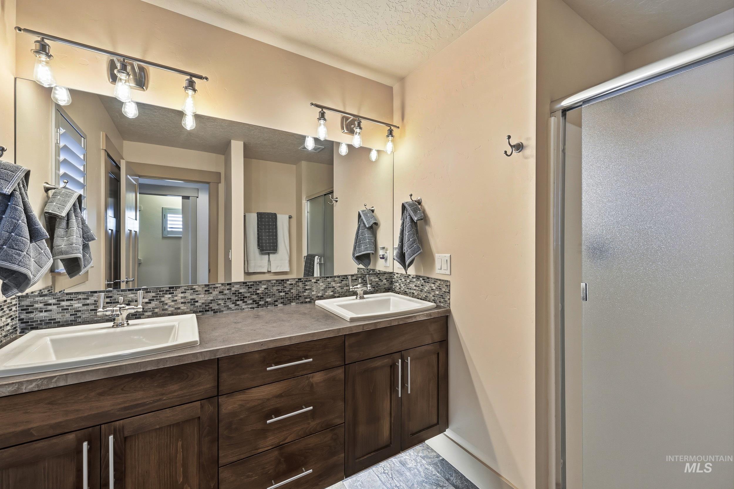 Bathroom with a textured ceiling, double vanity, a stall shower, and tasteful backsplash