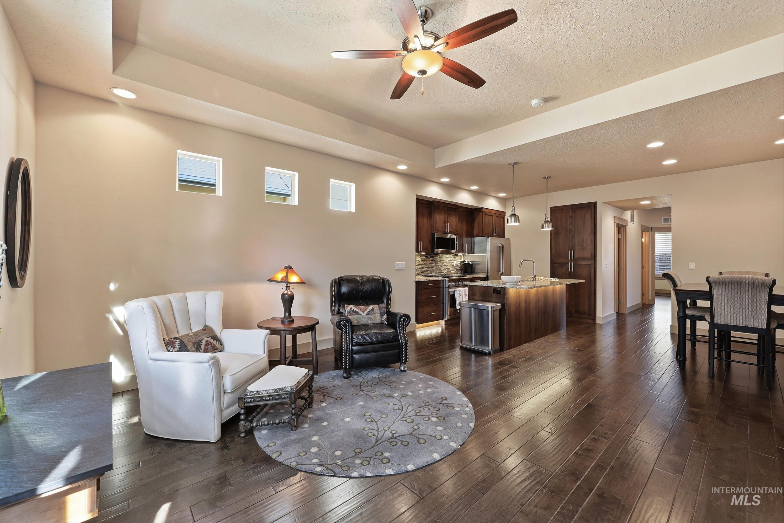 Living room with recessed lighting, plenty of natural light, dark wood-style floors, a ceiling fan, and a textured ceiling