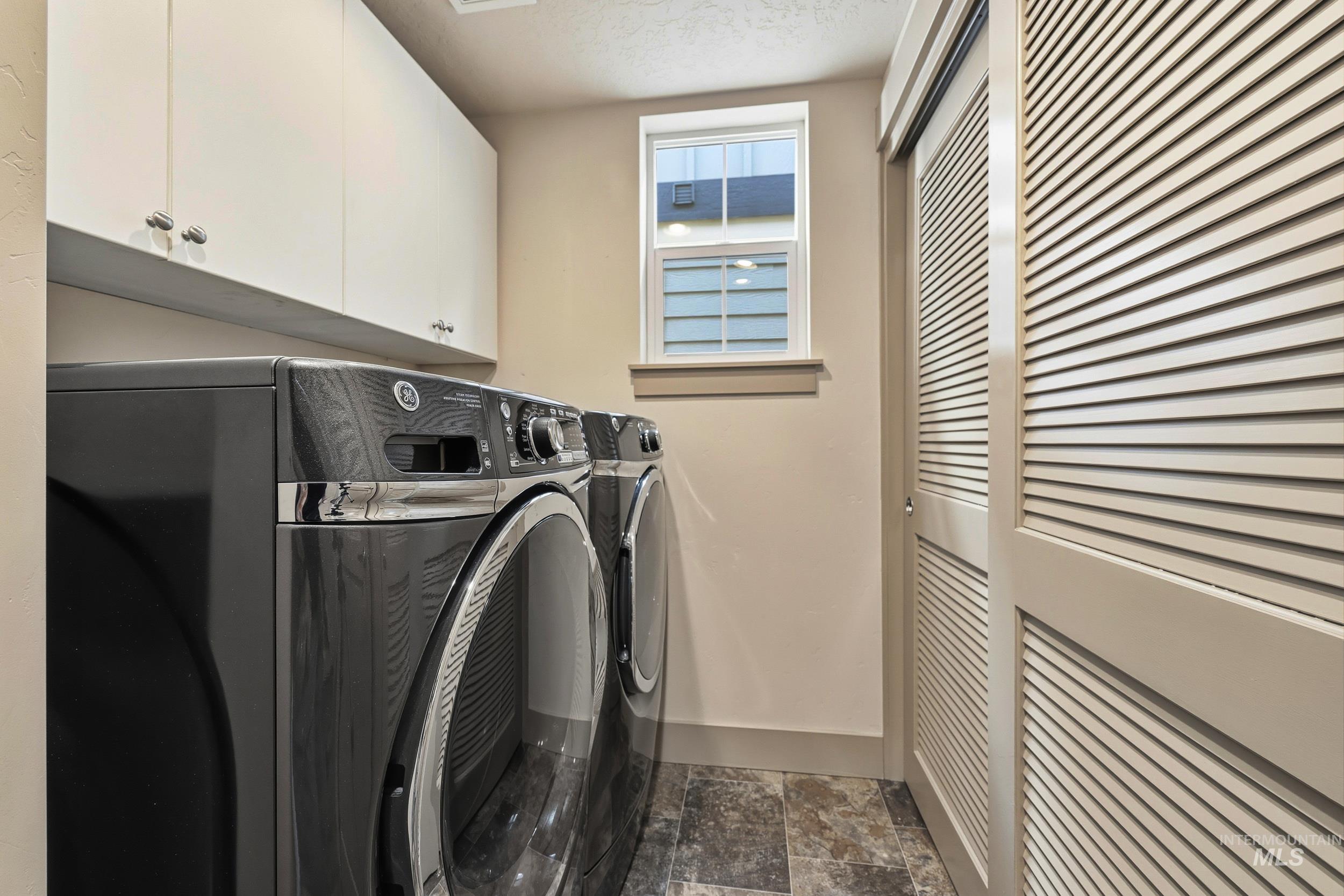 Laundry area featuring separate washer and dryer, cabinet space, a textured ceiling, and dark stone finish floors