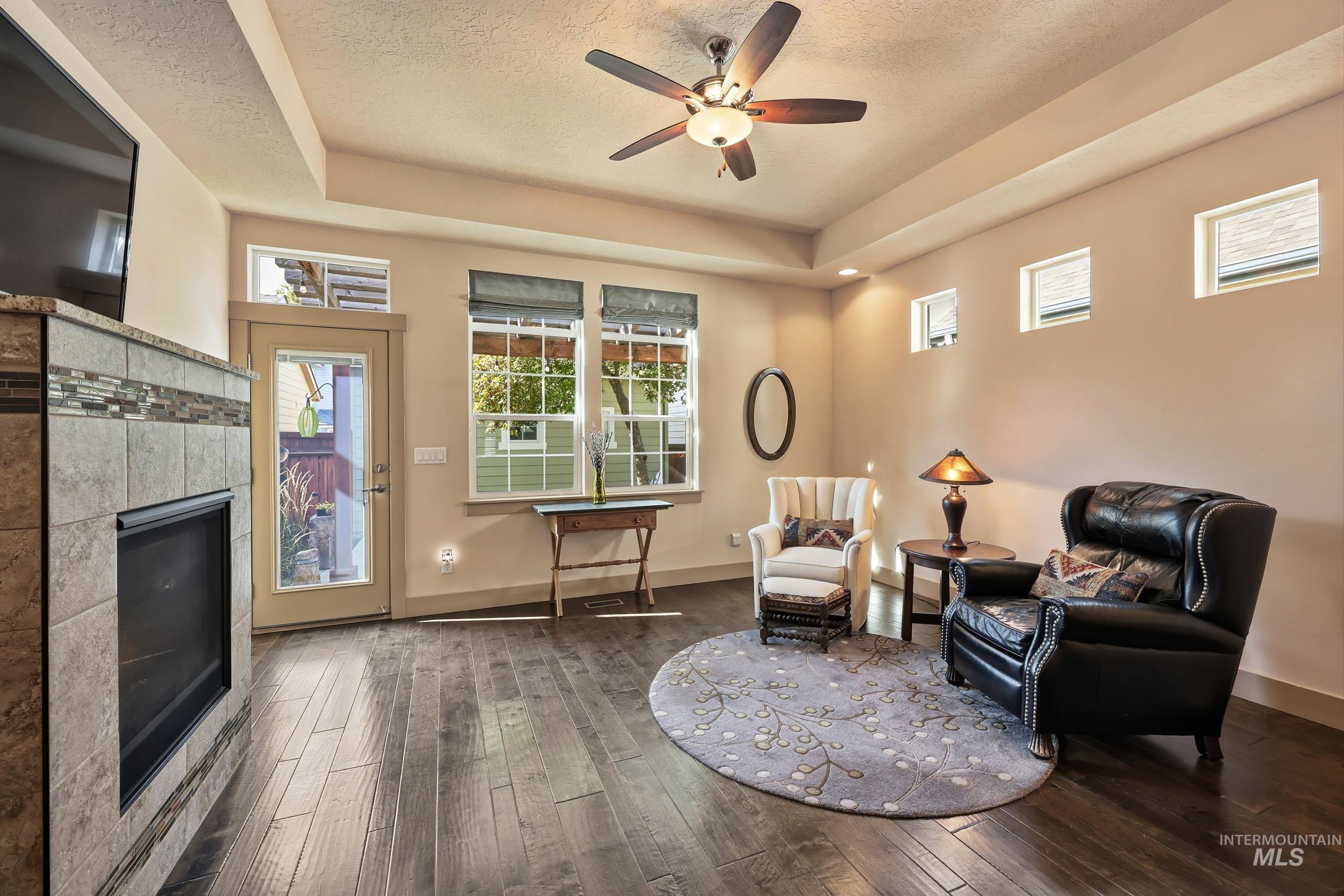 Sitting room featuring a fireplace, hardwood / wood-style floors, a raised ceiling, a ceiling fan, and a textured ceiling