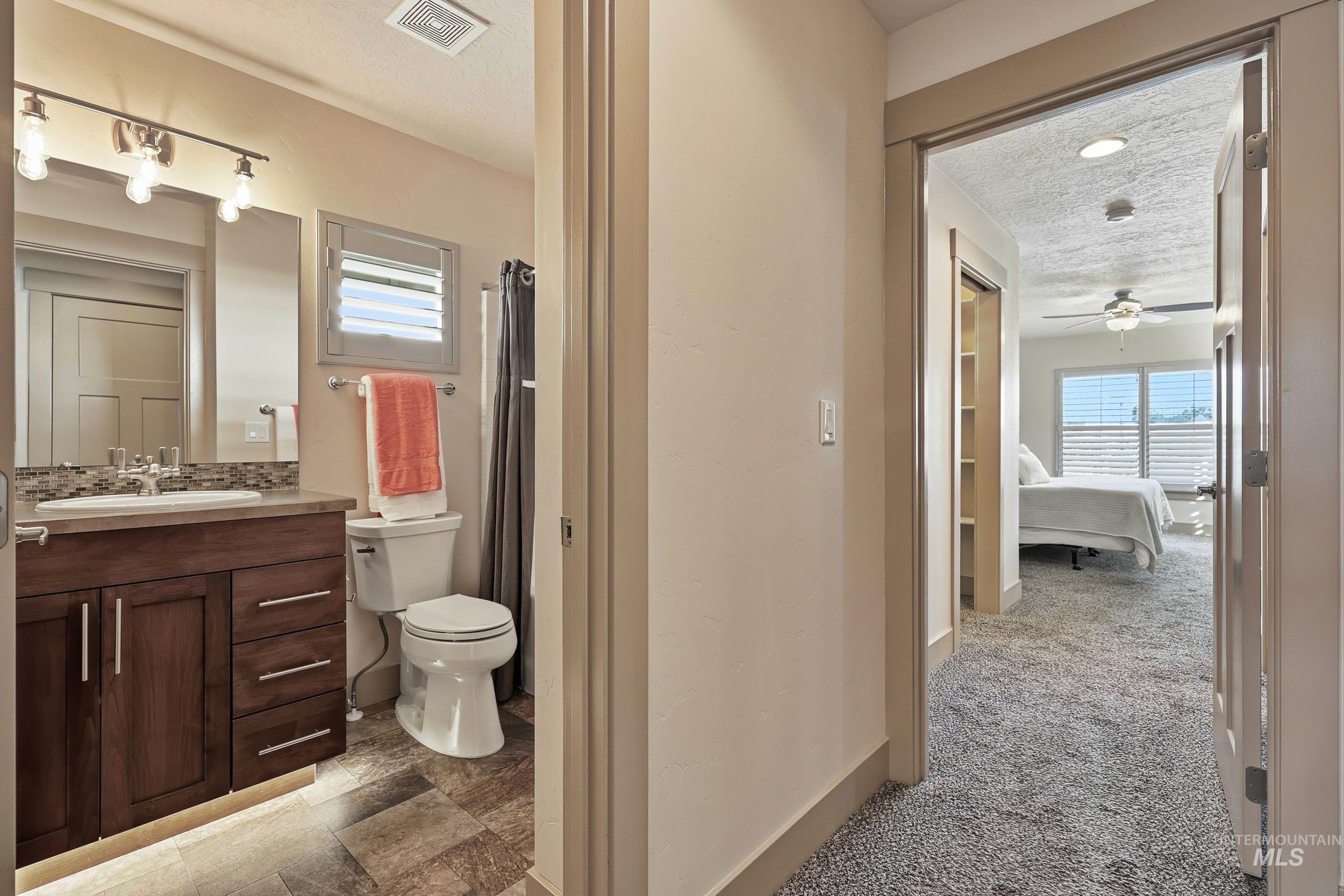 Ensuite bathroom featuring curtained shower, vanity, healthy amount of natural light, a textured ceiling, and decorative backsplash