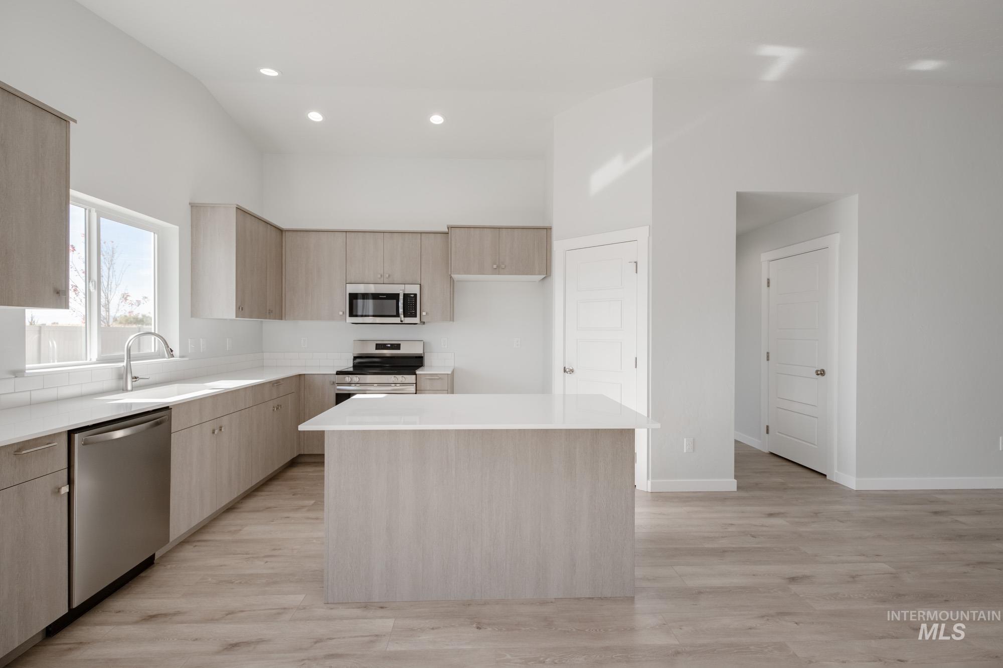 Kitchen with light brown cabinetry, modern cabinets, appliances with stainless steel finishes, recessed lighting, and light stone counters