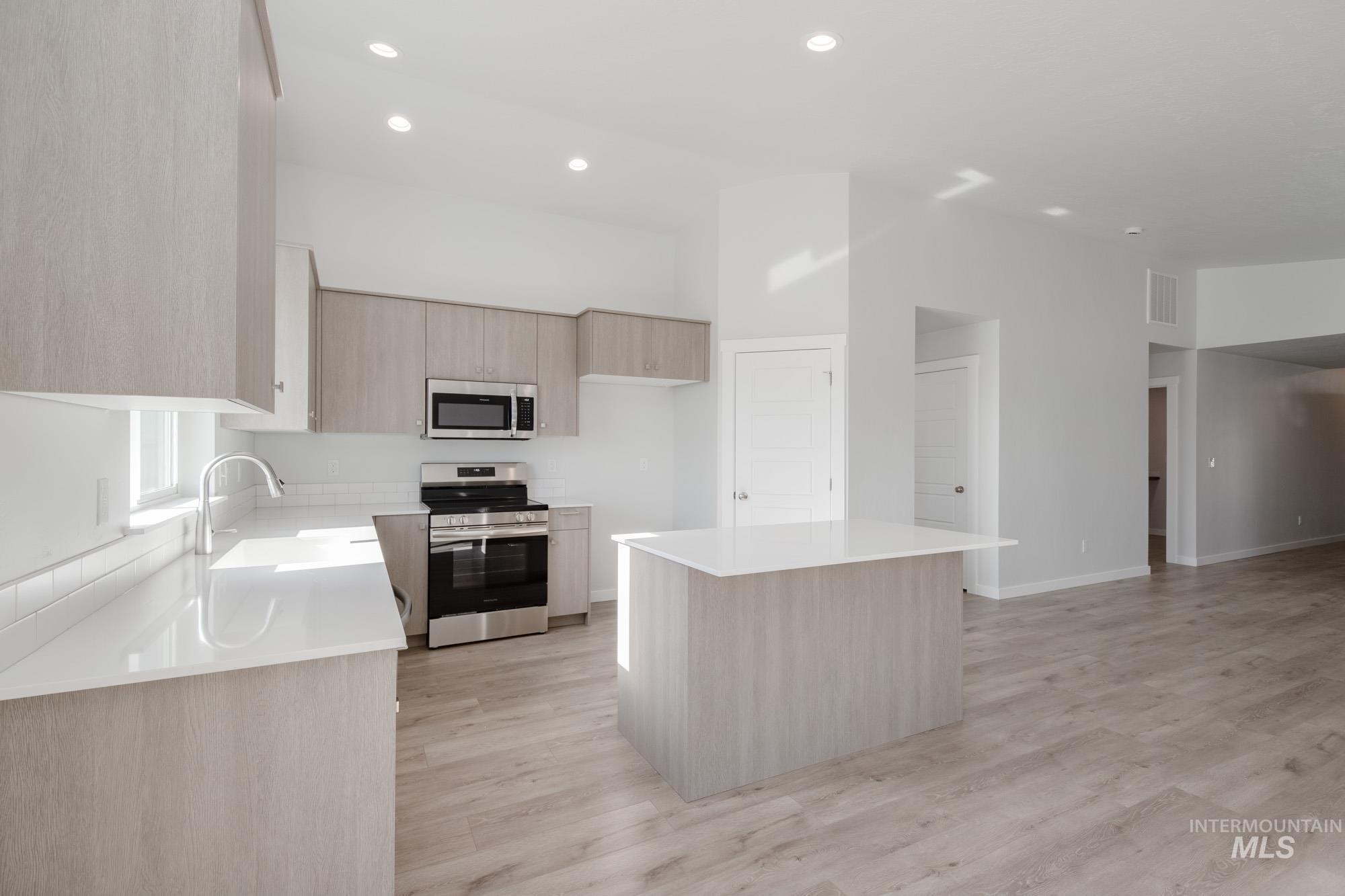 Kitchen featuring light brown cabinetry, appliances with stainless steel finishes, a kitchen island, light wood-style flooring, and recessed lighting