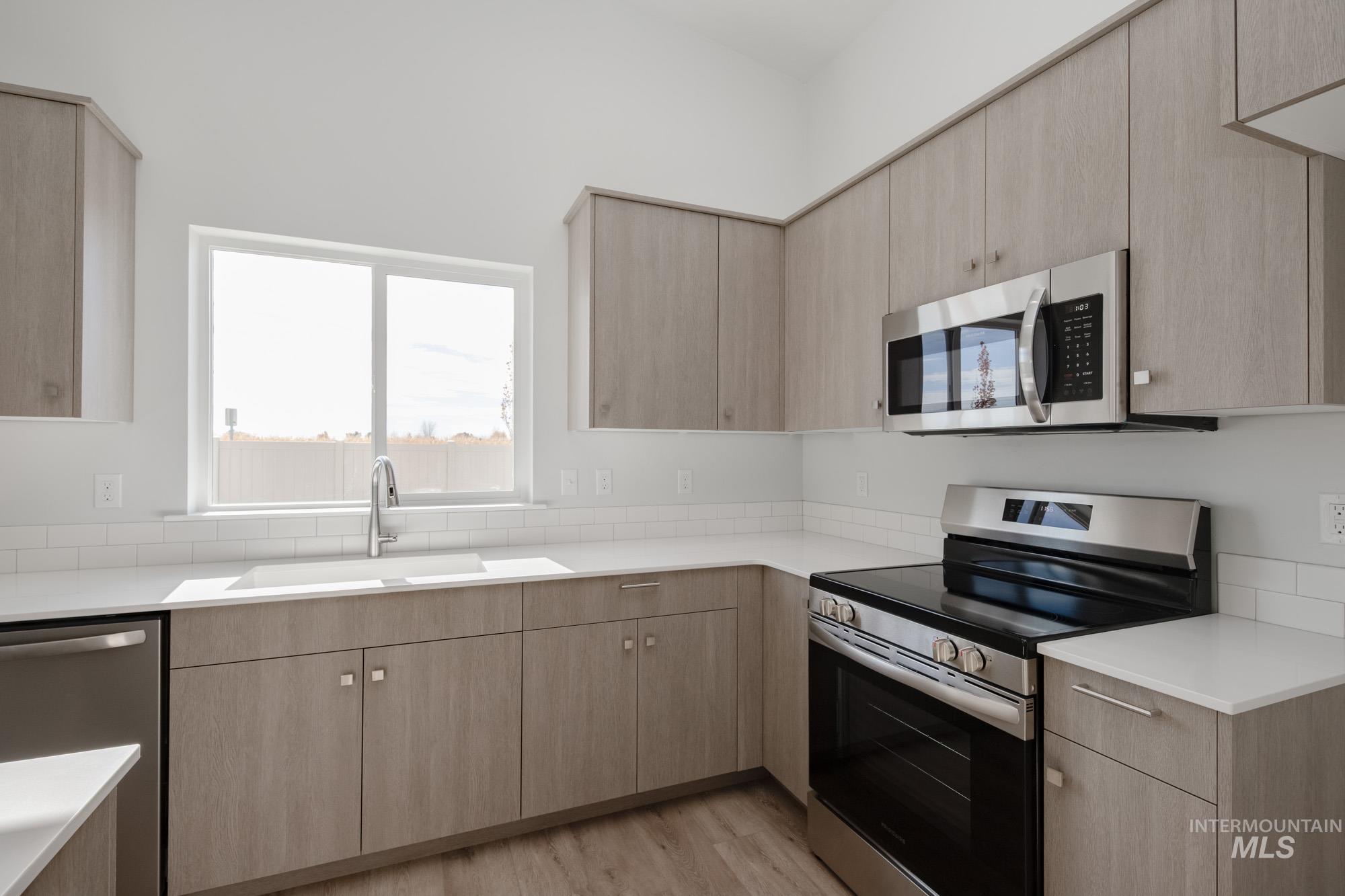 Kitchen featuring stainless steel appliances, light brown cabinetry, light wood-style floors, modern cabinets, and light stone counters